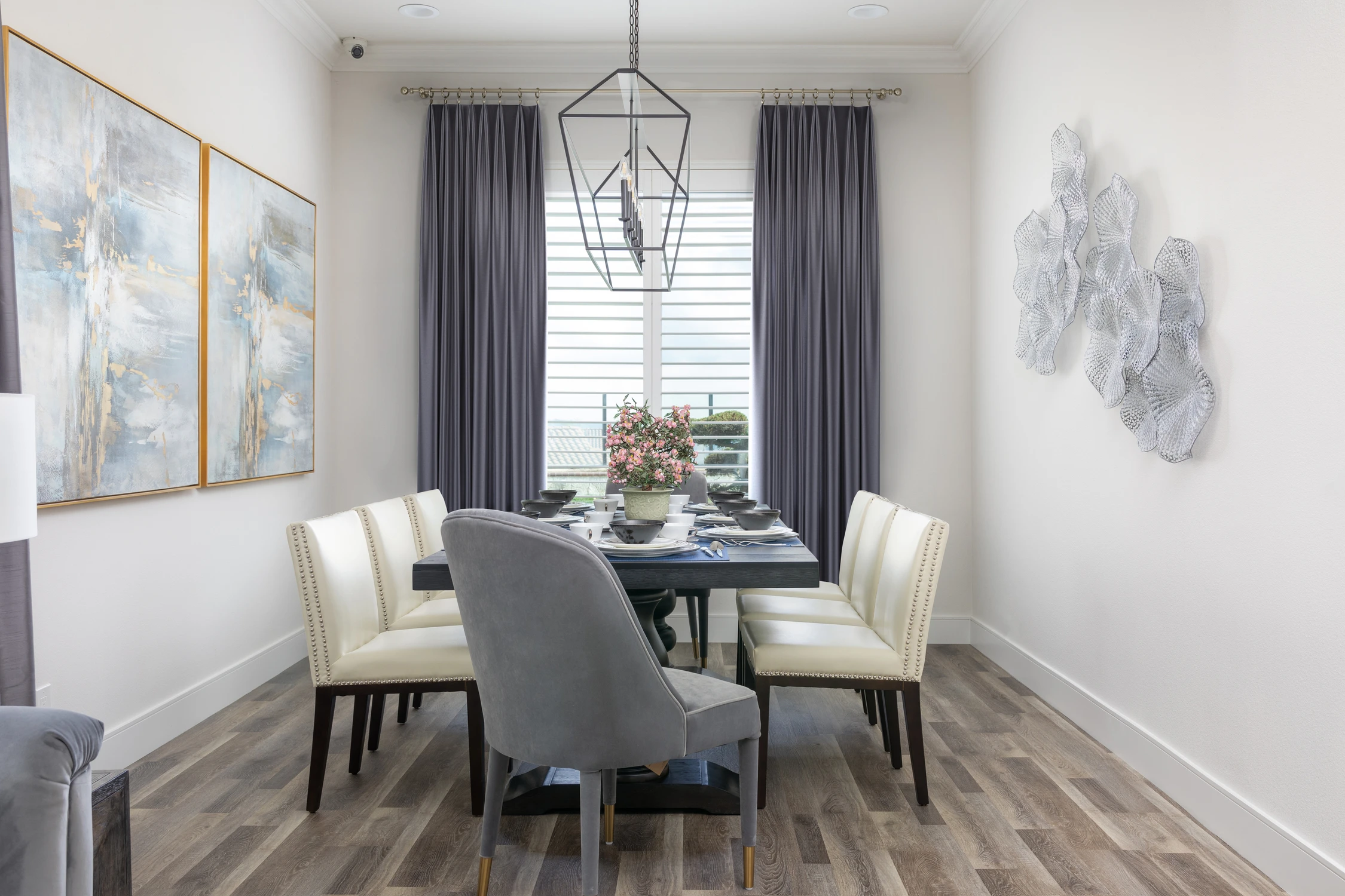 Formal dining room with blue artwork, gray drapery, and a black chandelier