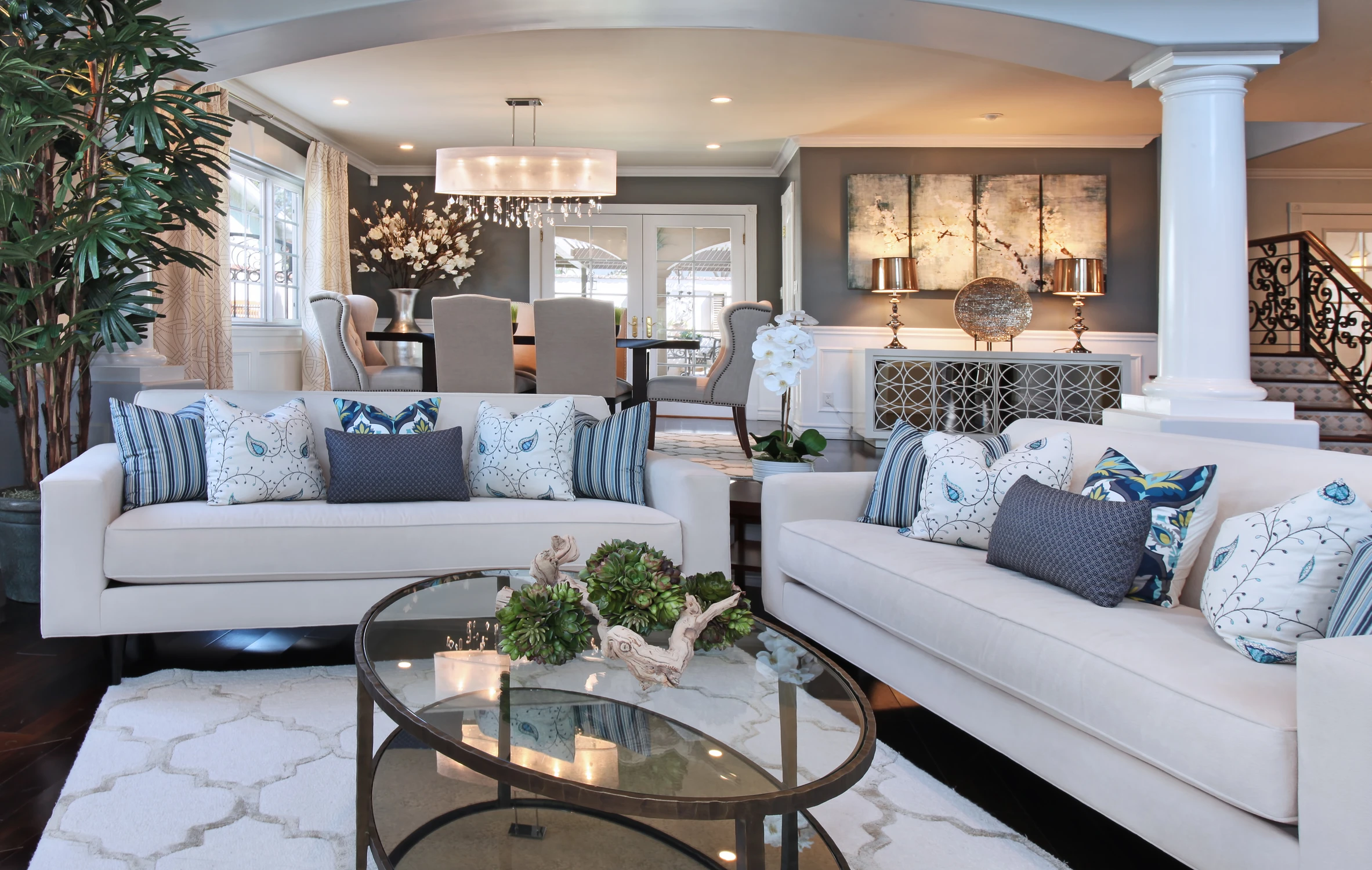 Family room with white sofas, glass coffee table, and columned opening