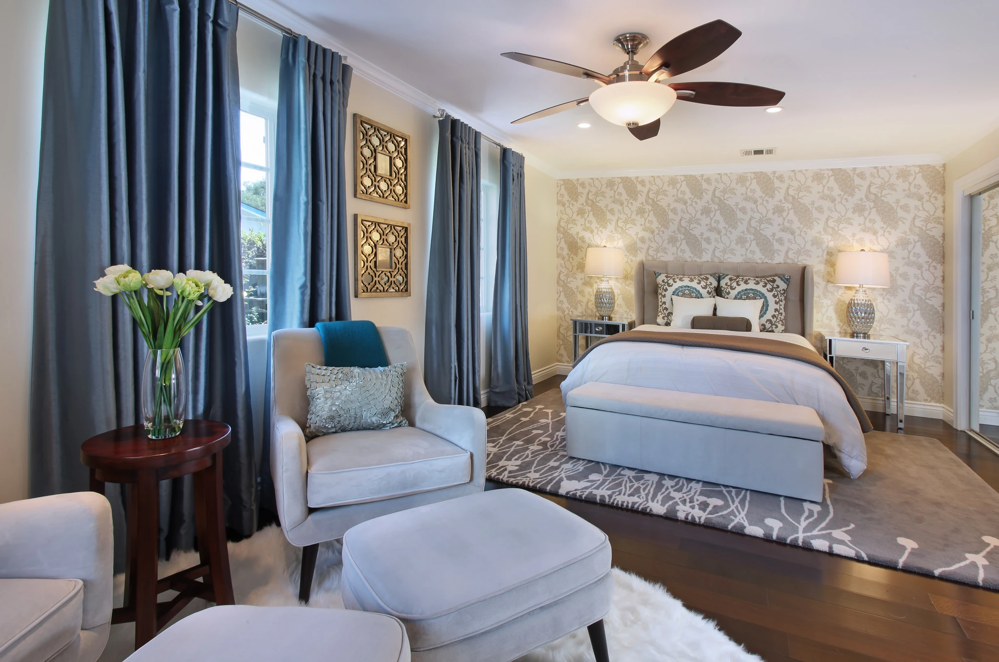 Bedroom with blue curtains, pale upholstered bed, and patterned wallpaper