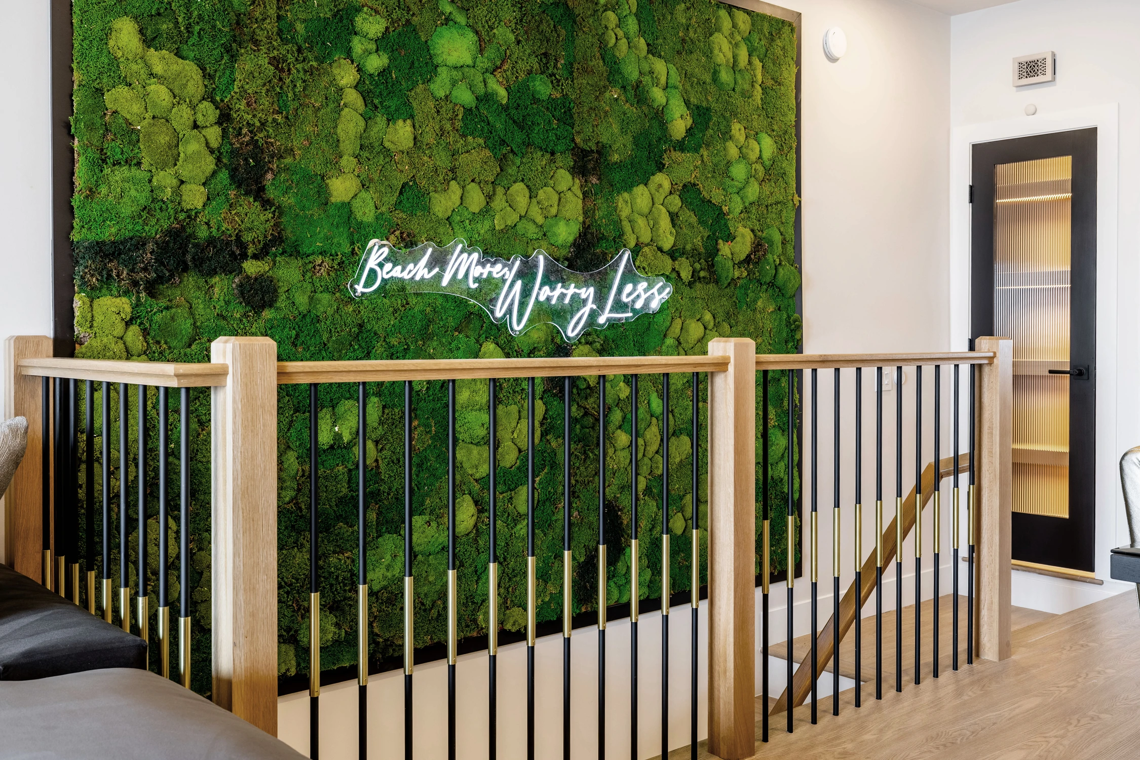 Moss wall sign above gold railing and black stair balusters