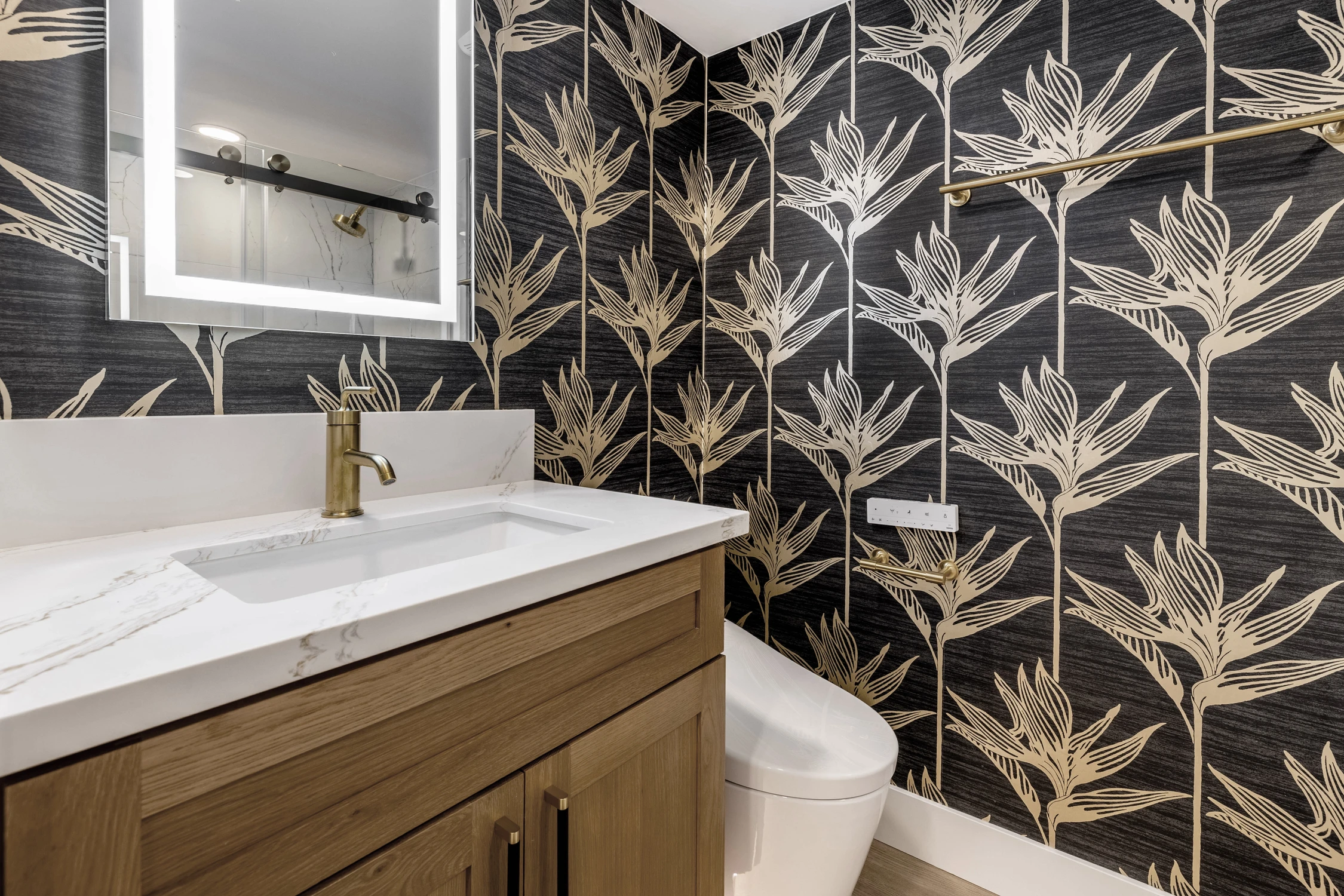 Powder room with botanical wallpaper, wood vanity, and brass faucet