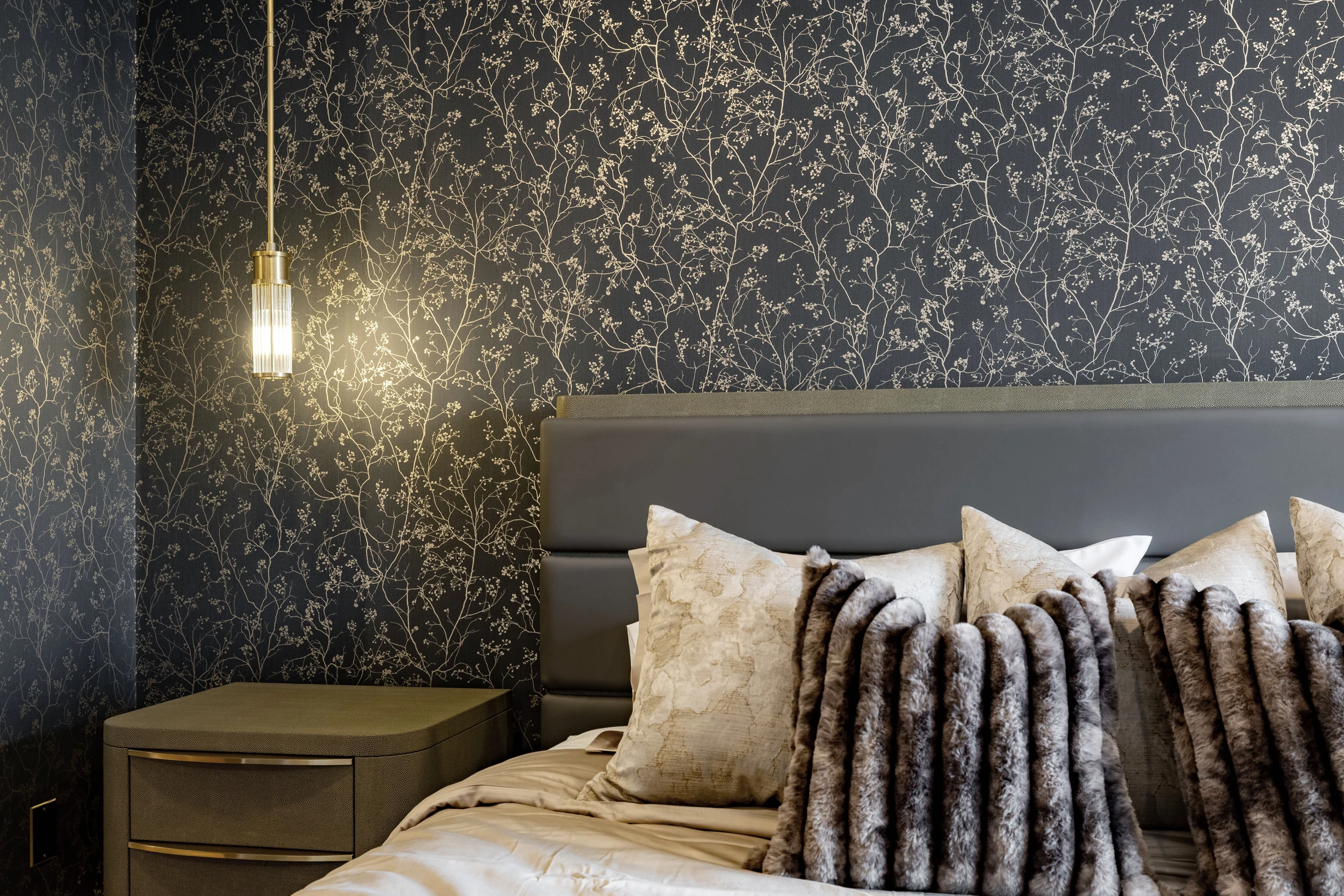 Bedroom with dark botanical wallcovering, upholstered bed, and brass pendant
