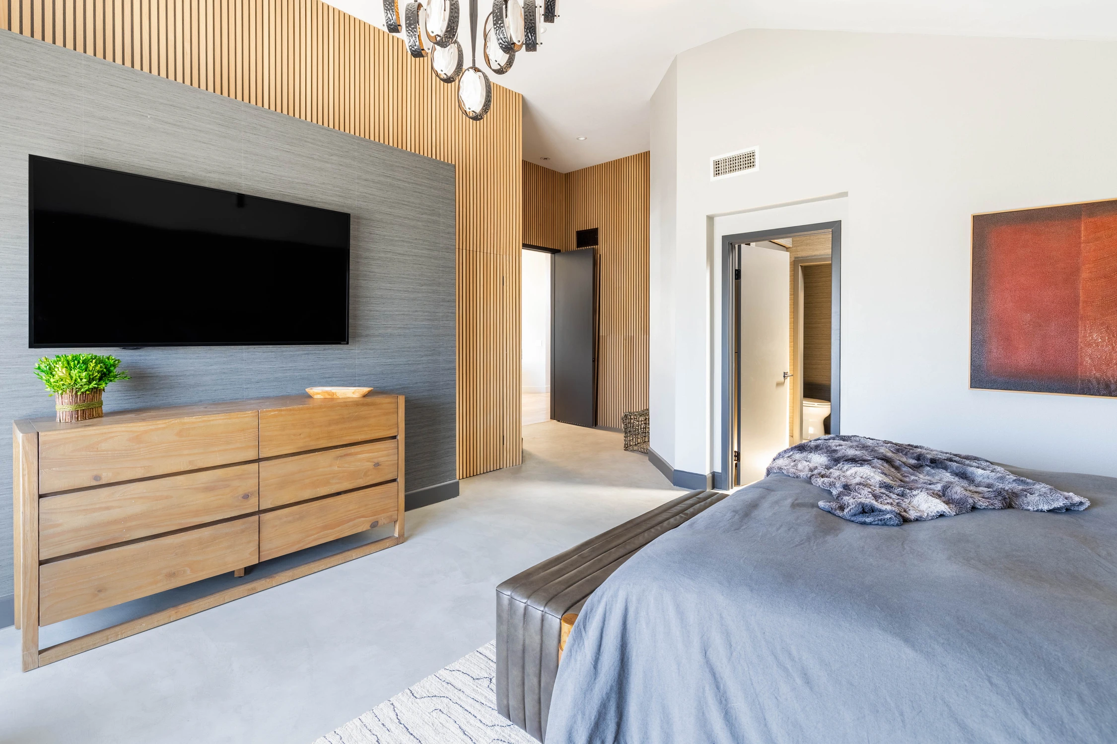 Bedroom media wall with pale wood dresser and geometric chandelier
