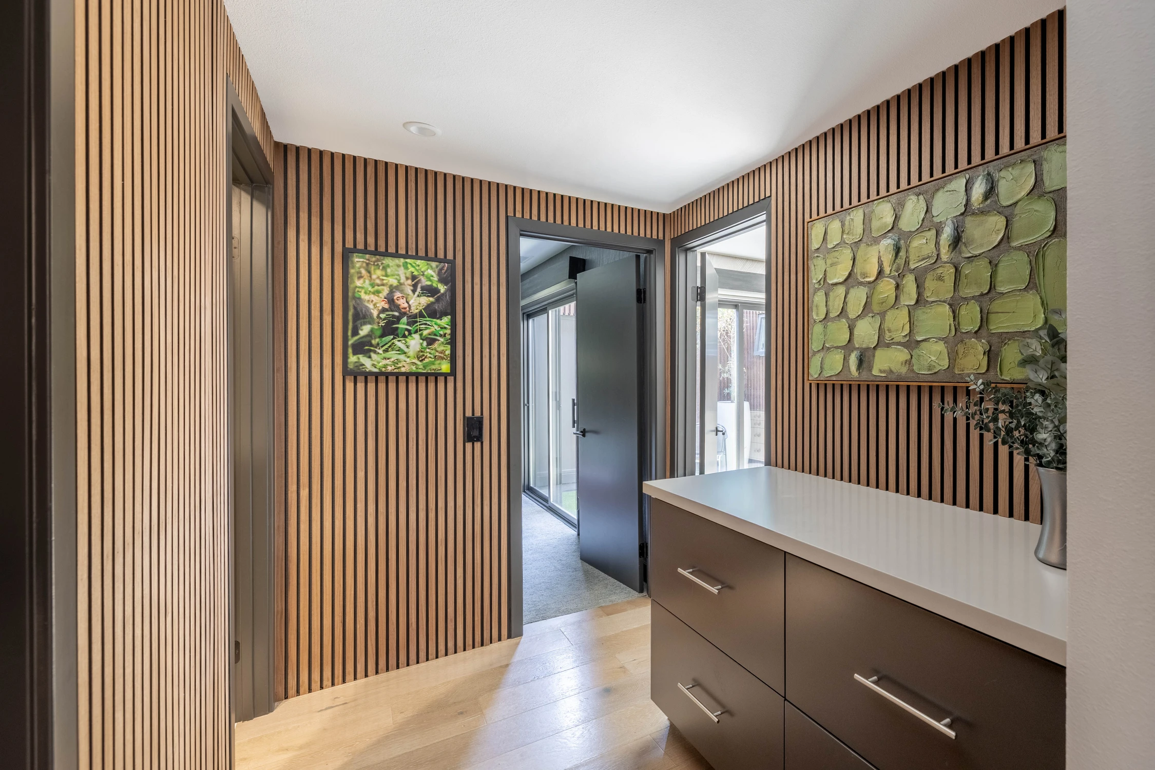 Hallway with wood slat walls, dark doors, and low cabinet
