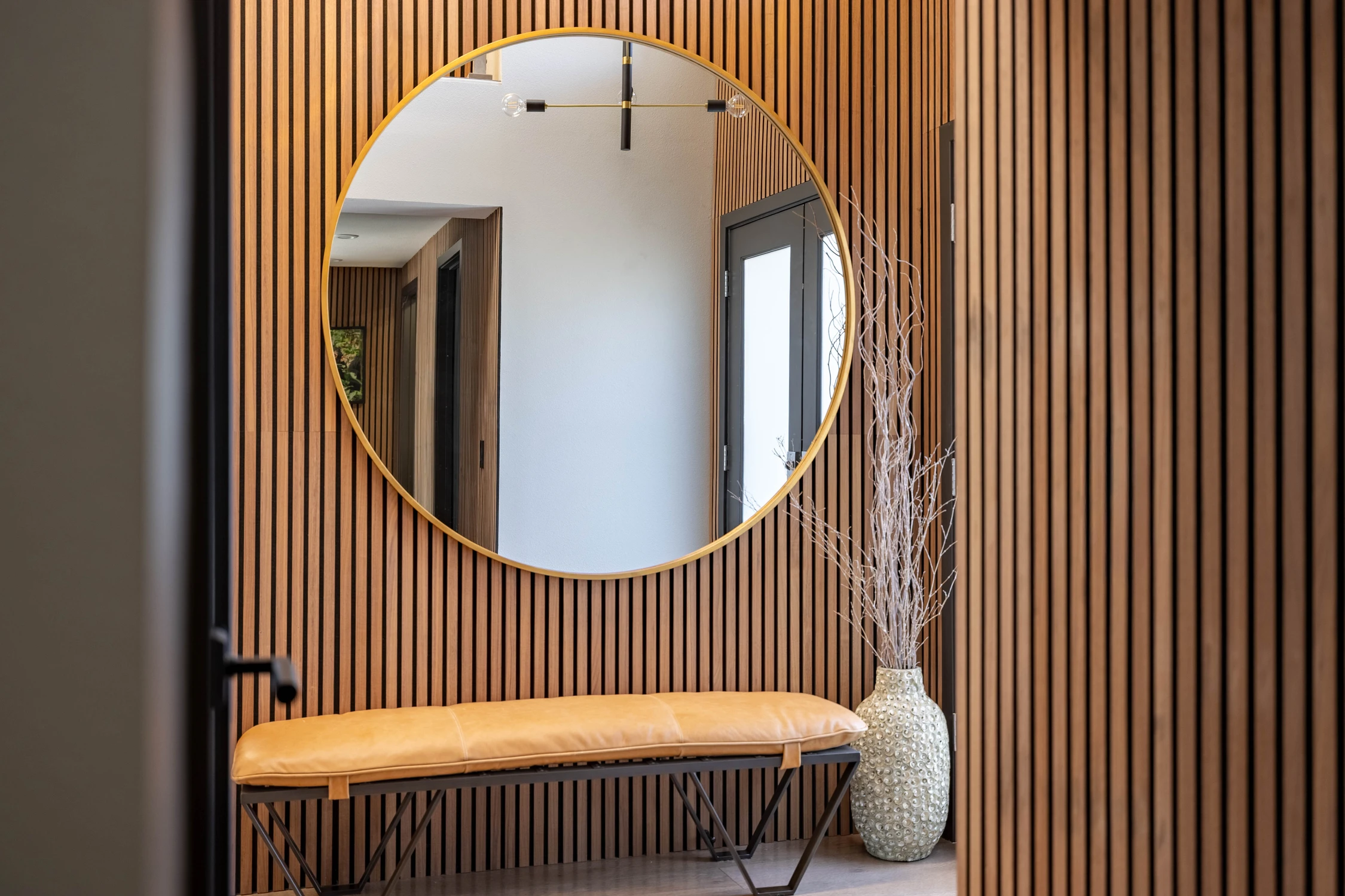 Bedroom with round mirror above a wood console and slatted wall