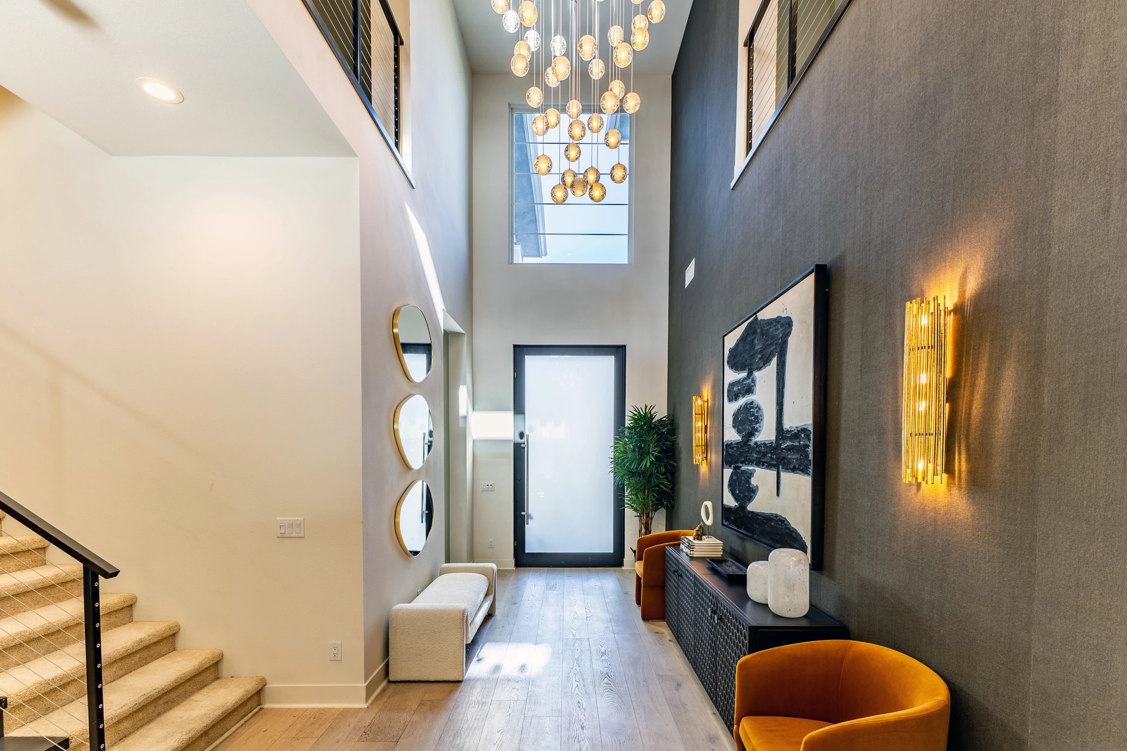 Double-height entryway with pendant chandelier, dark accent wall, and mustard chairs