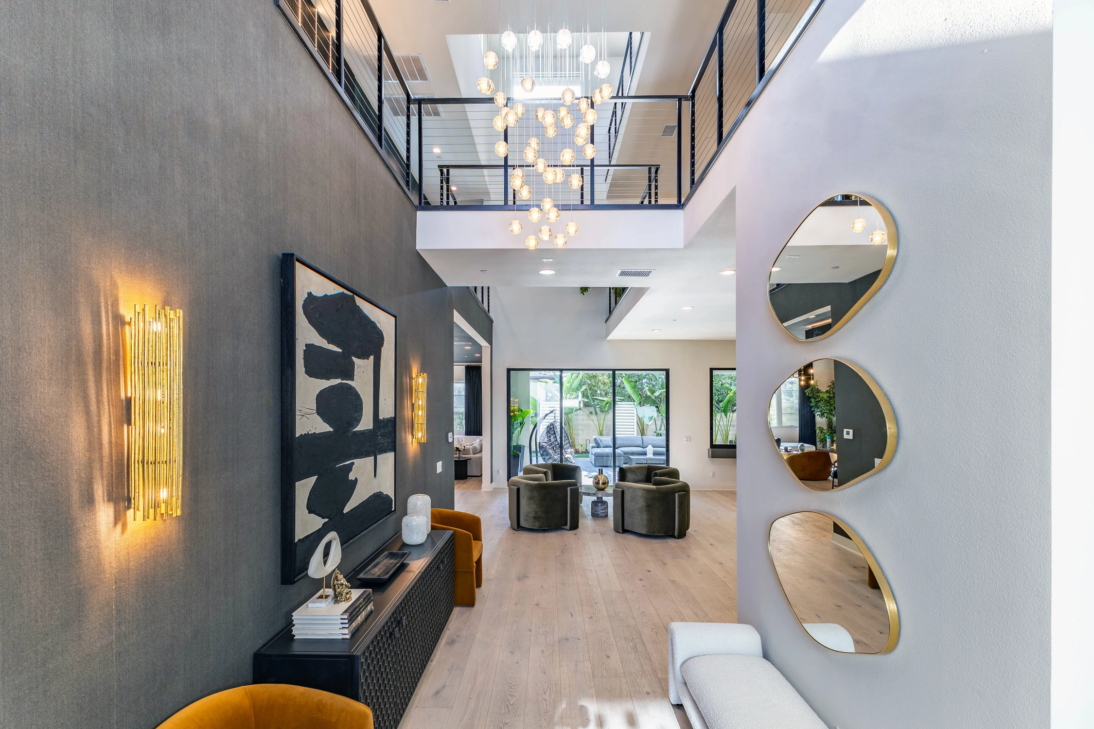 Double-height entryway with chandeliers, black railing, and round mirrors