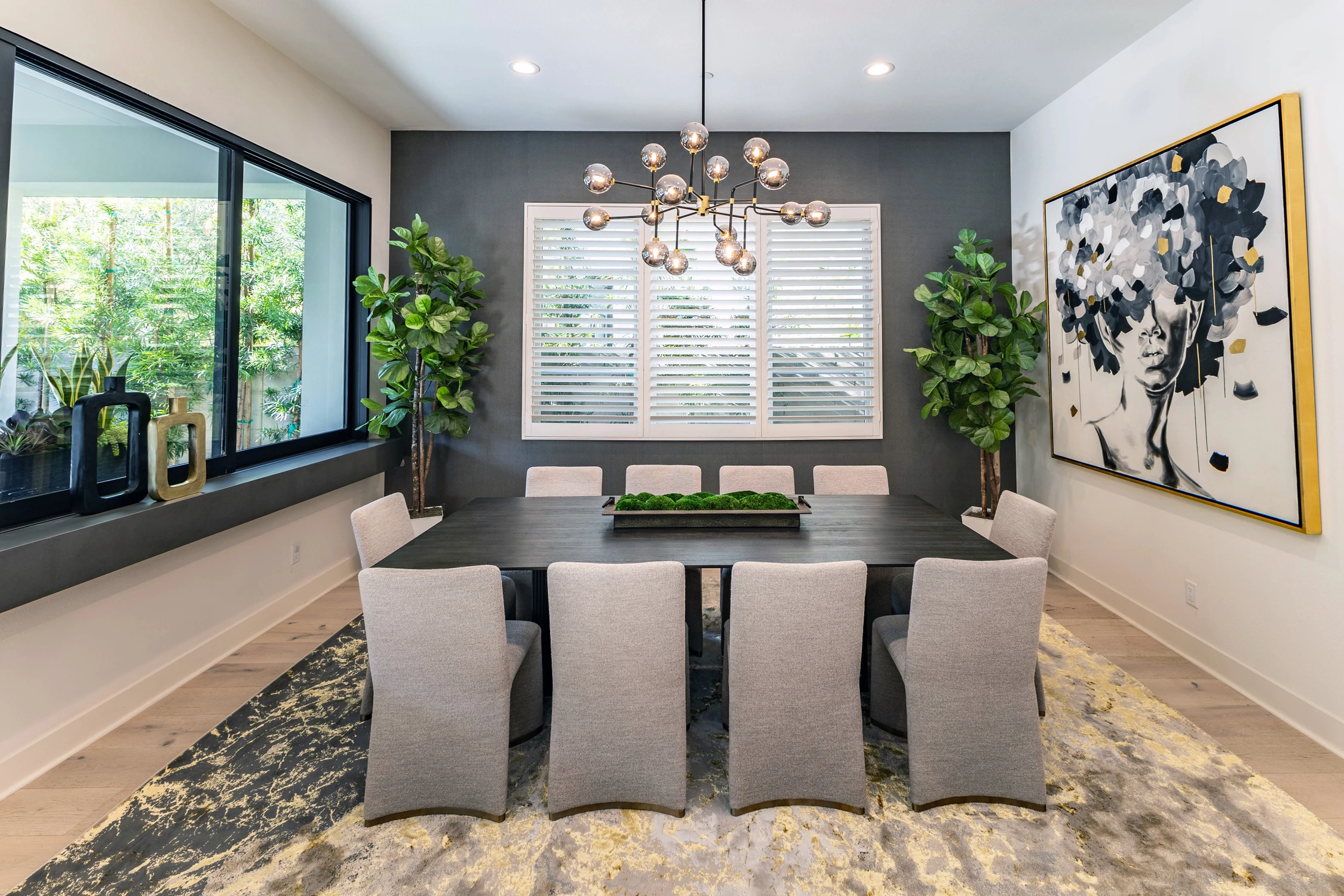 Dining room with long black table, upholstered chairs, and dark accent wall
