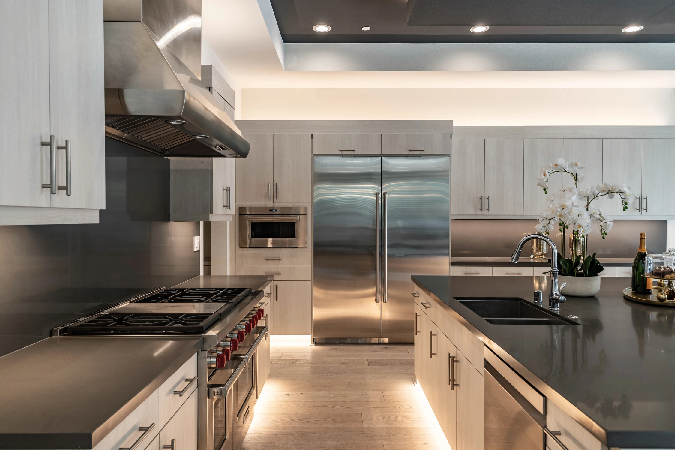Kitchen with pale wood cabinetry, stainless appliances, and black counters