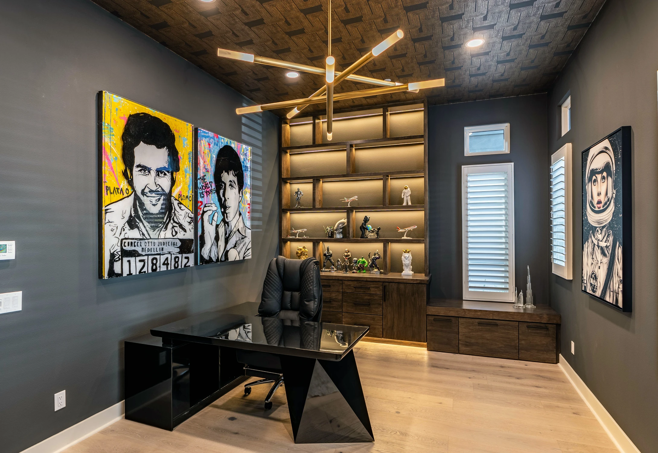 Home office with black desk, lighted wood shelving, and pop-art portraits