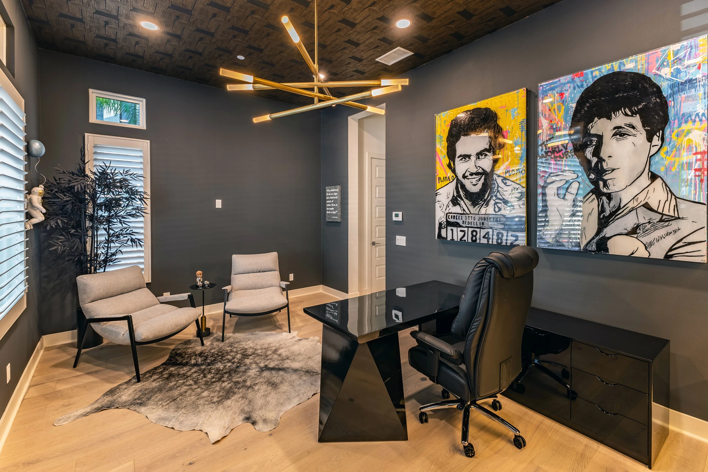 Home office with black desk, lounge chairs, and pop-art portraits