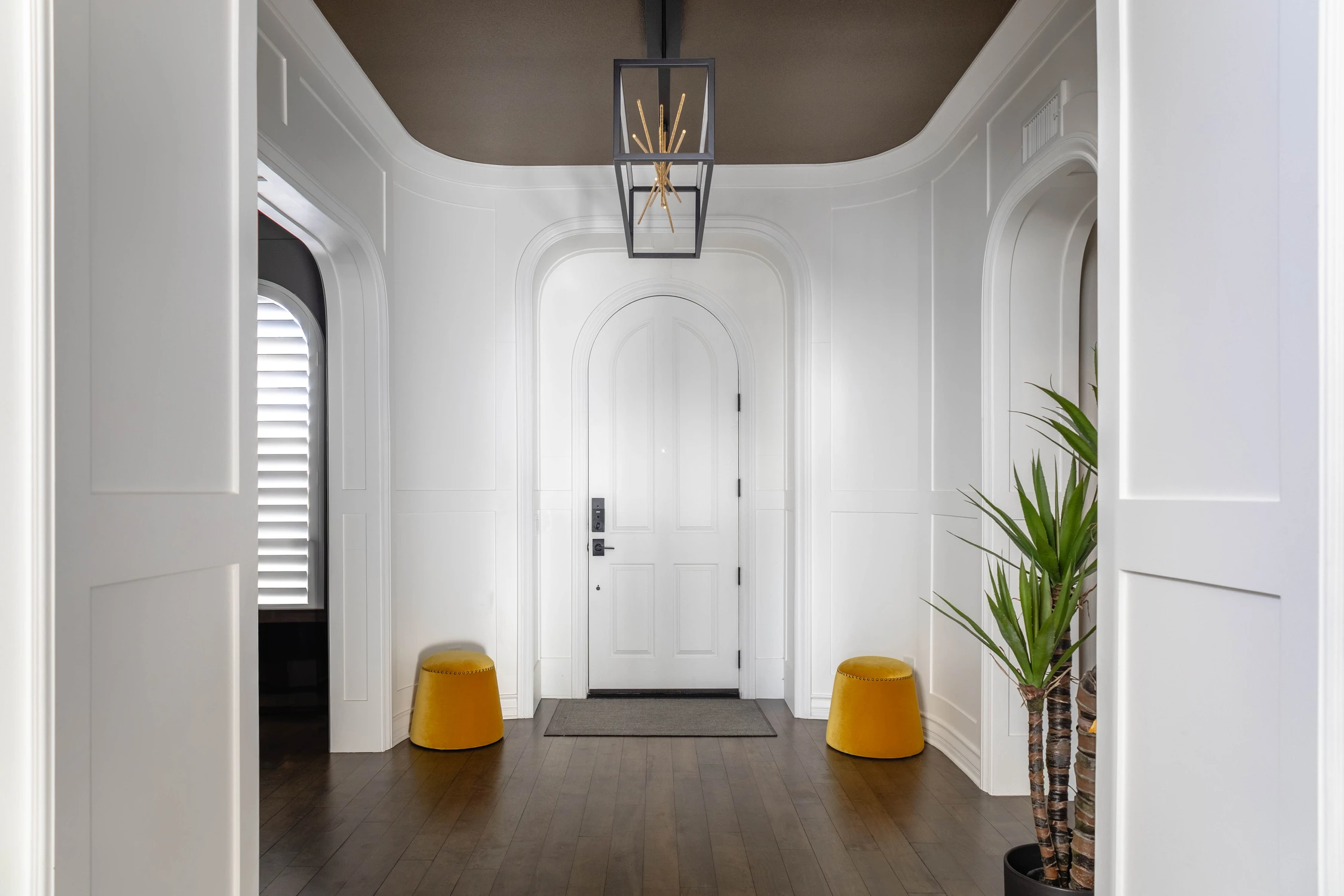 White entry hall with arched doorway and mustard stools