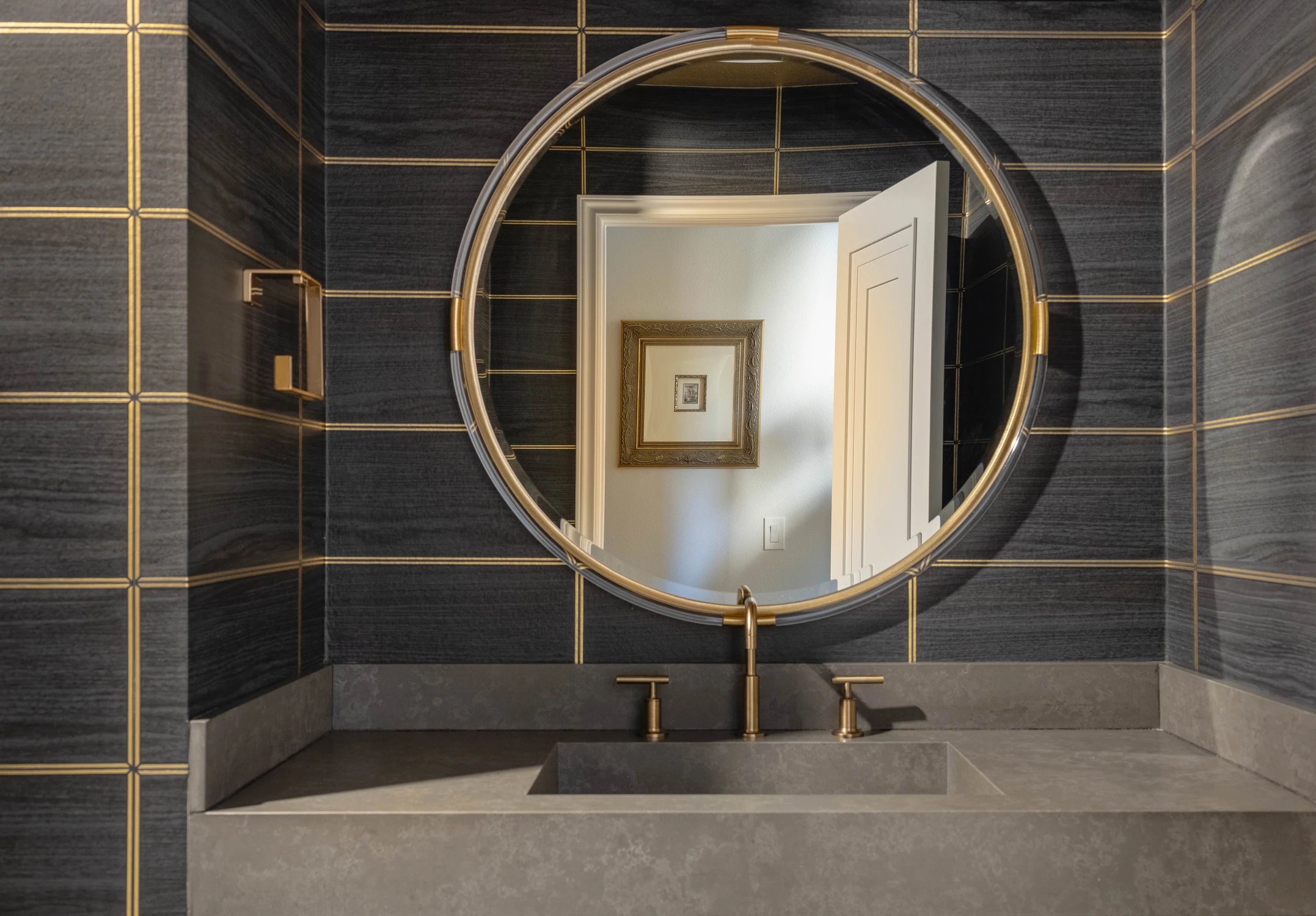 Round brass-framed mirror on black tiled powder room wall