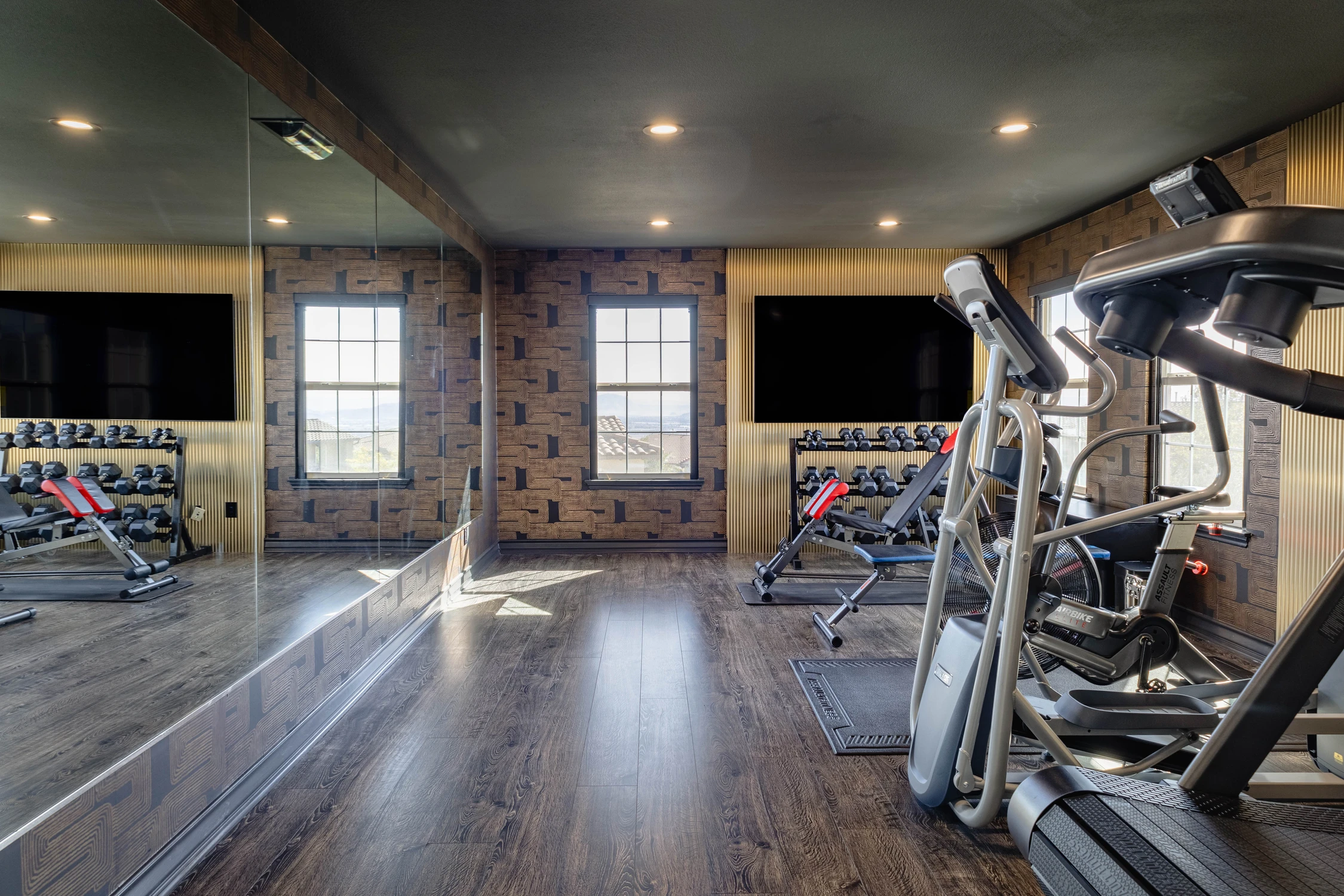 Home gym with mirrored wall, exercise equipment, and televisions