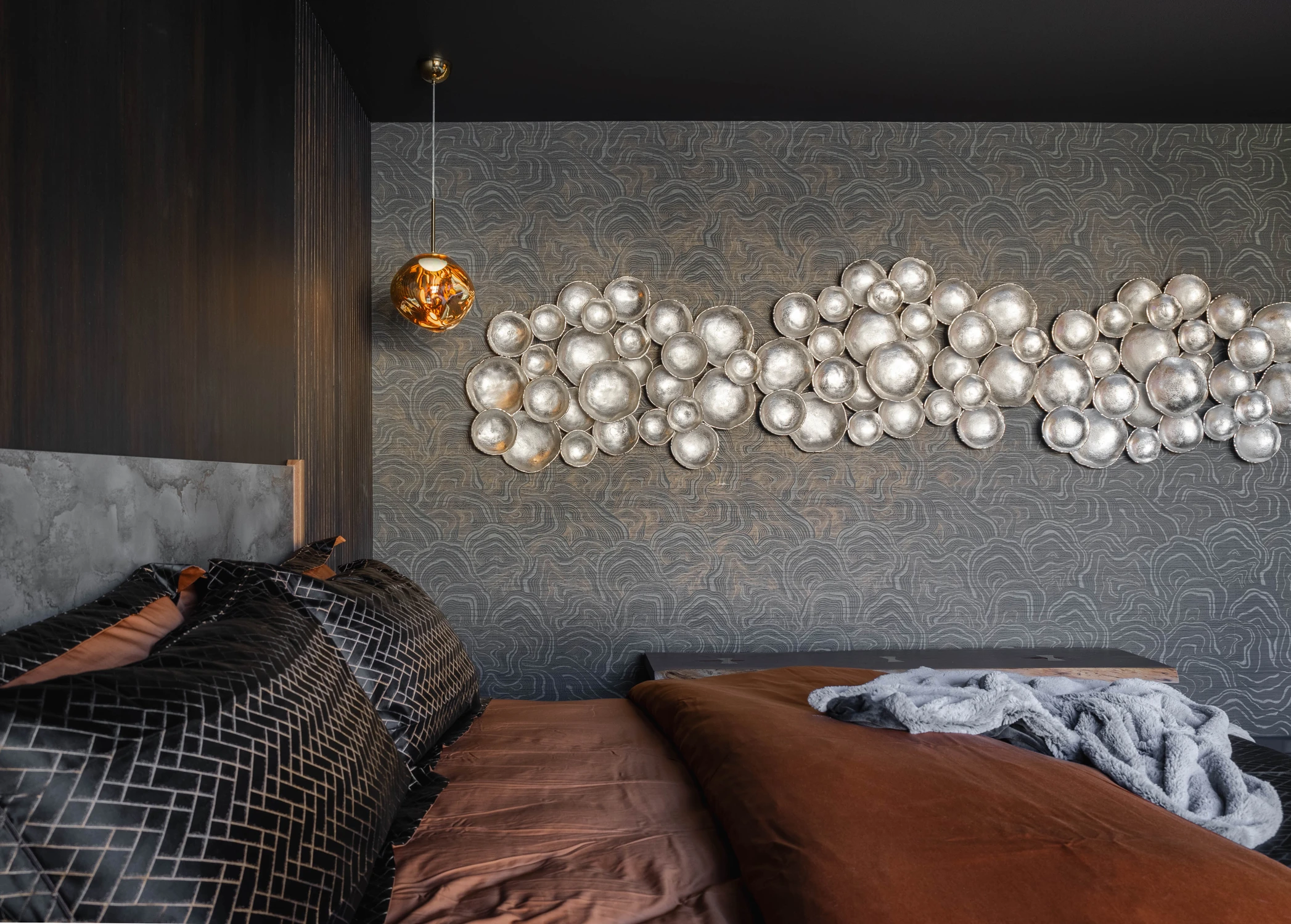 Dark bedroom wall with metallic sculpture and amber pendant