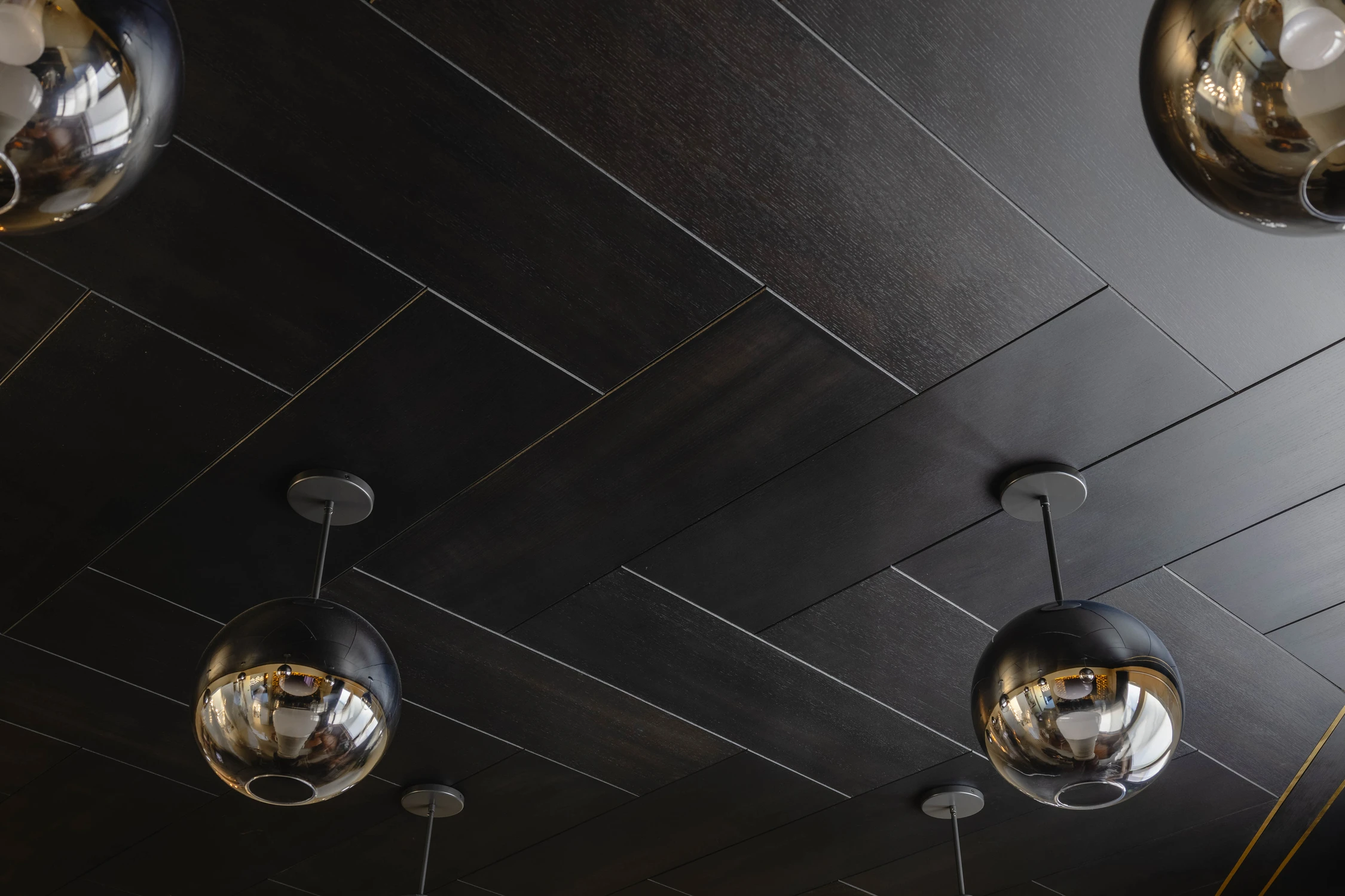 Herringbone wood ceiling with gold metal border and reflective globe pendant lights