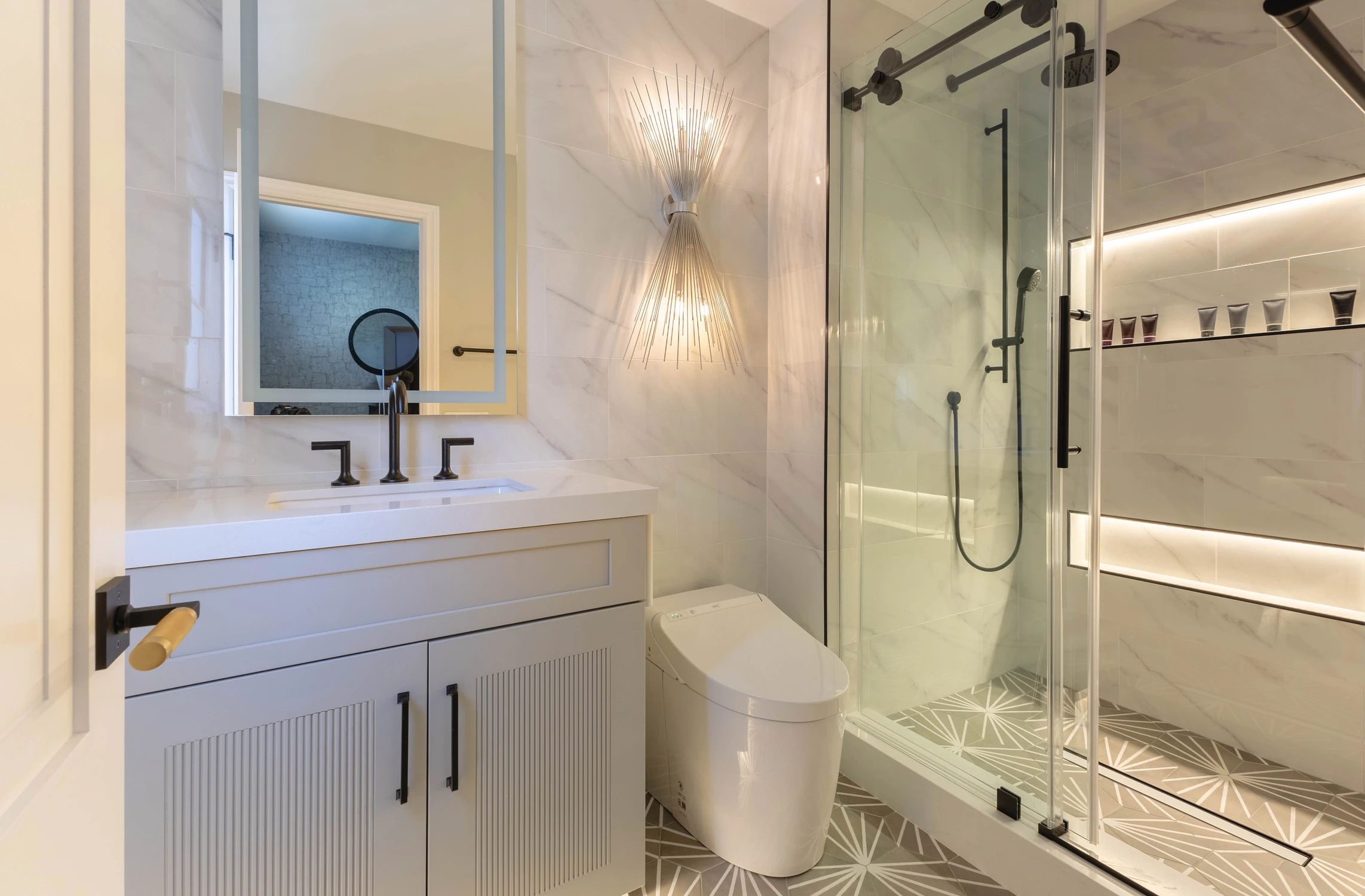 White bathroom vanity beside glass shower with illuminated niches