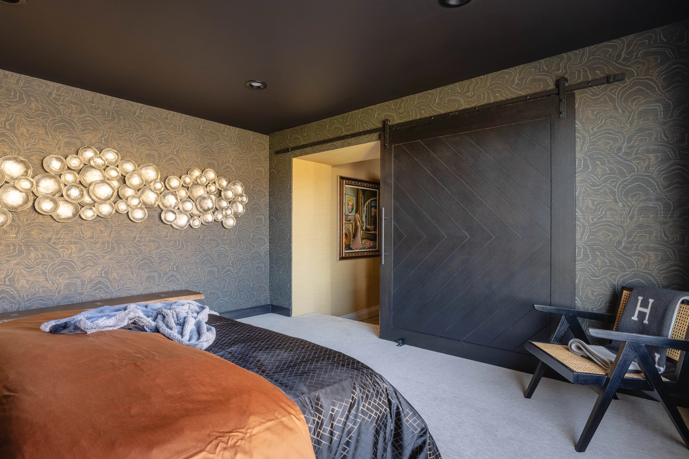 Dark bedroom with metallic wall sculpture and partially open sliding door