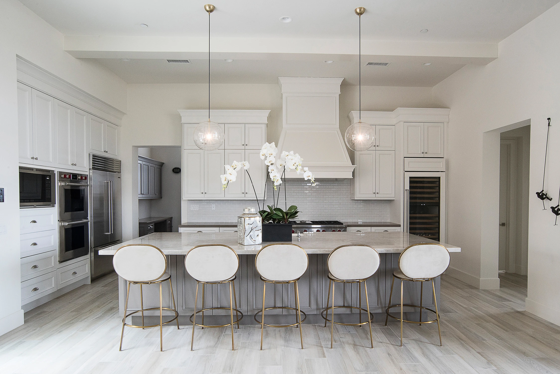 White kitchen with gray island, white stools, and globe pendants