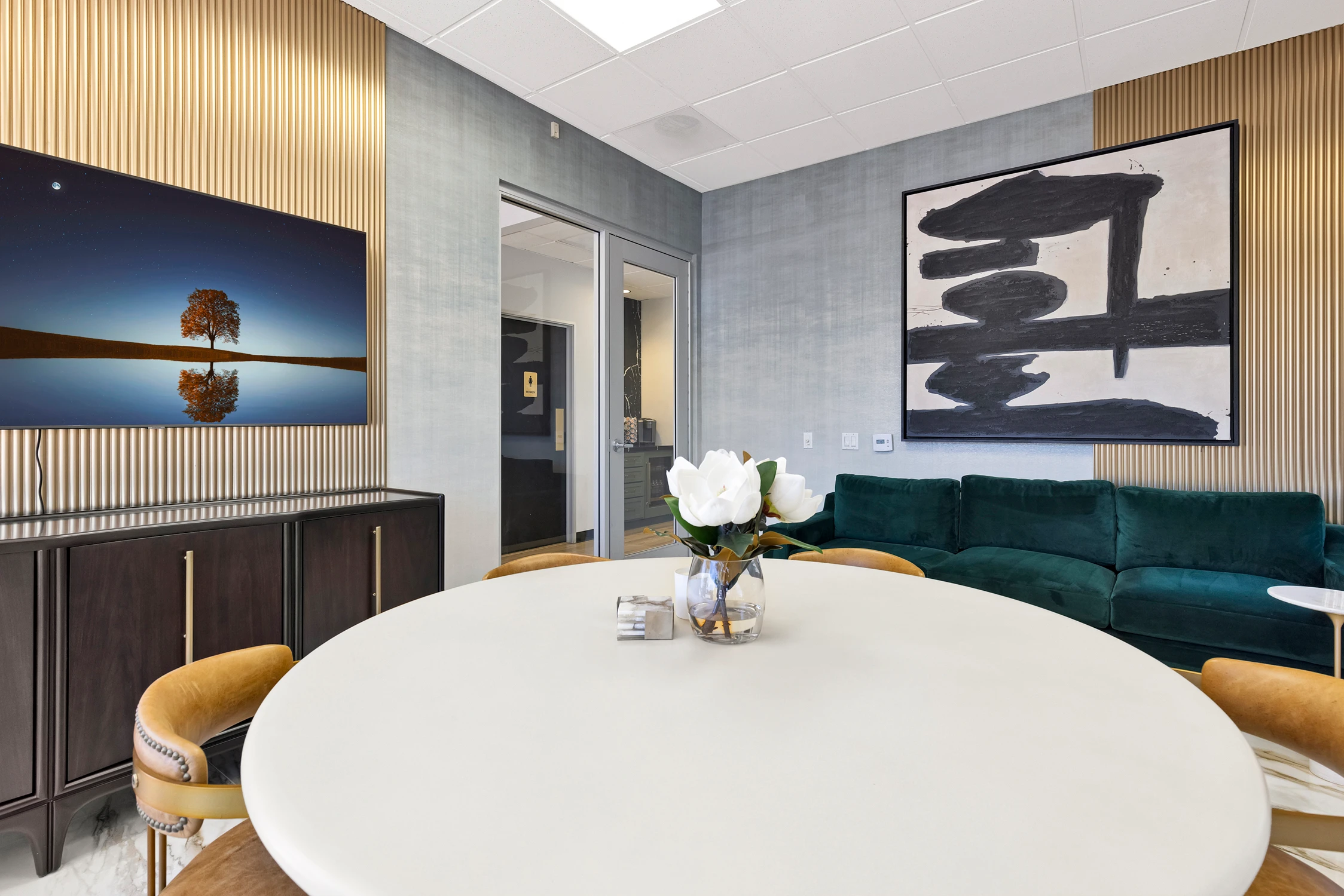 Office lounge with teal sectional, brass wall panels, and round table