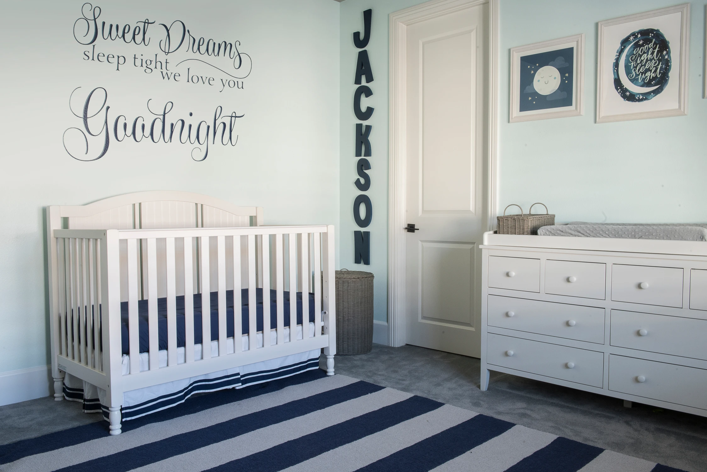 Nursery with white crib, navy striped rug, and personalized wall lettering