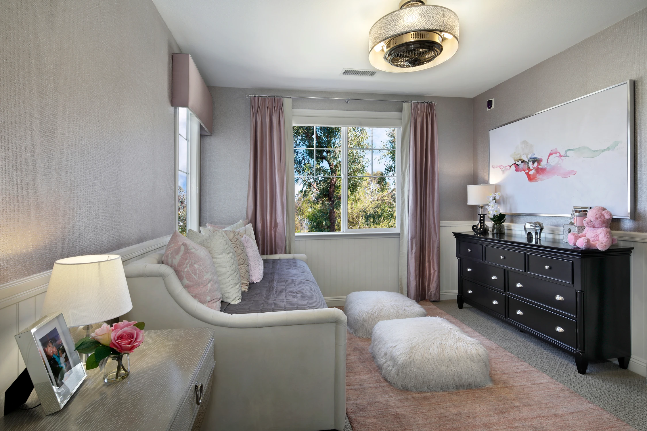 Bedroom with gray chaise lounge, pink curtains, and dark dresser