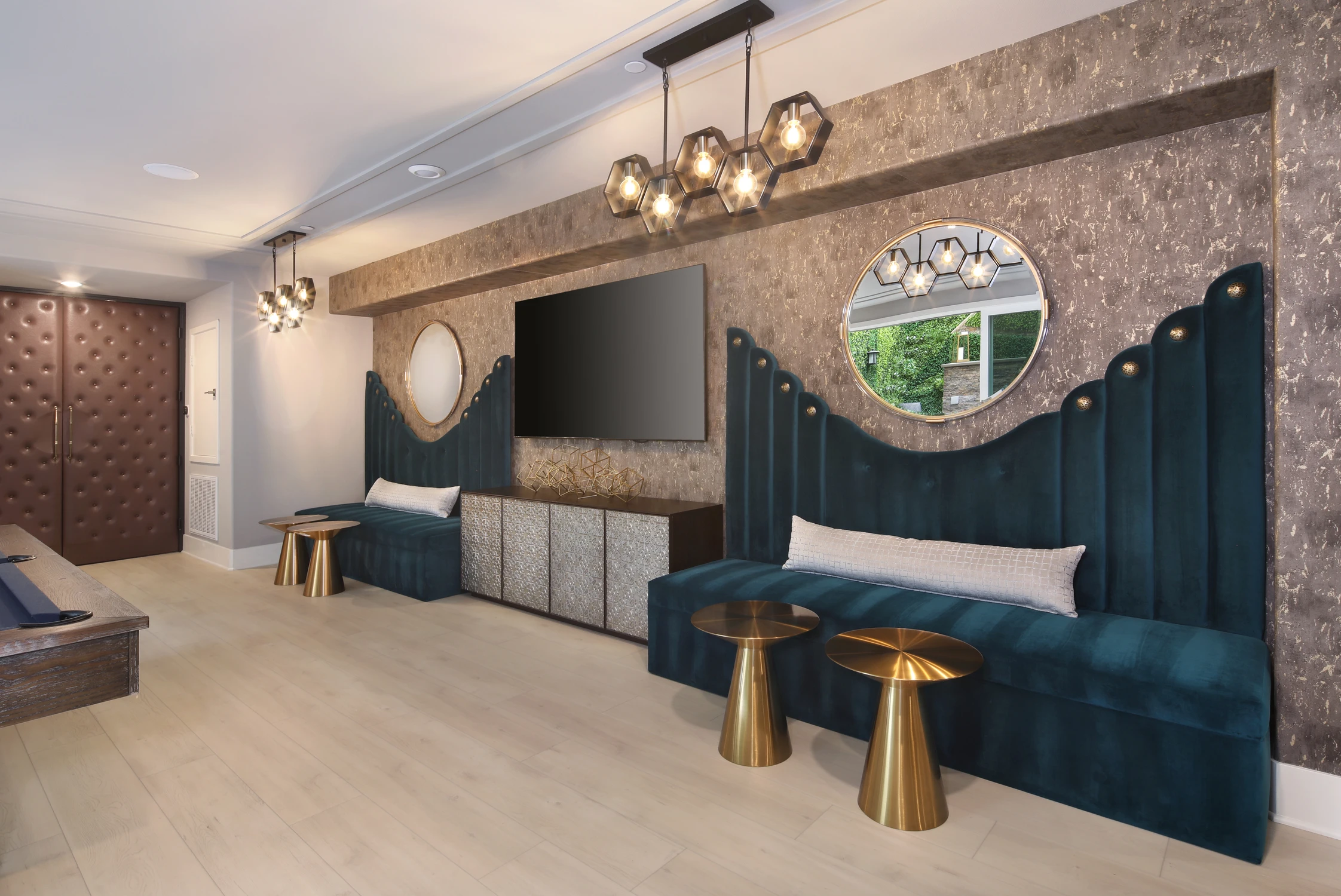 Teal banquette beside a round mirror and brass side tables