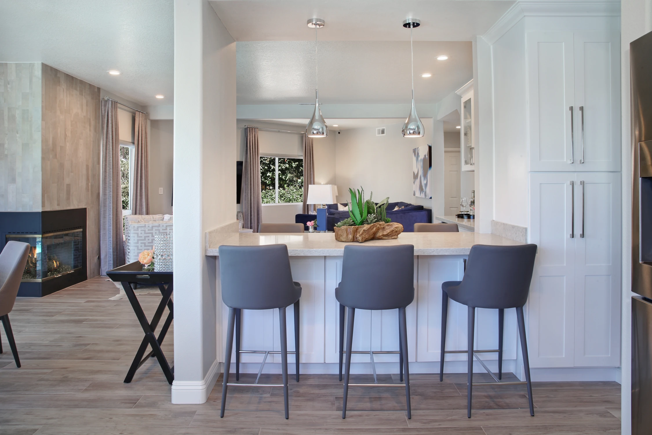 Open white kitchen and dining area with gray stools and wood floors