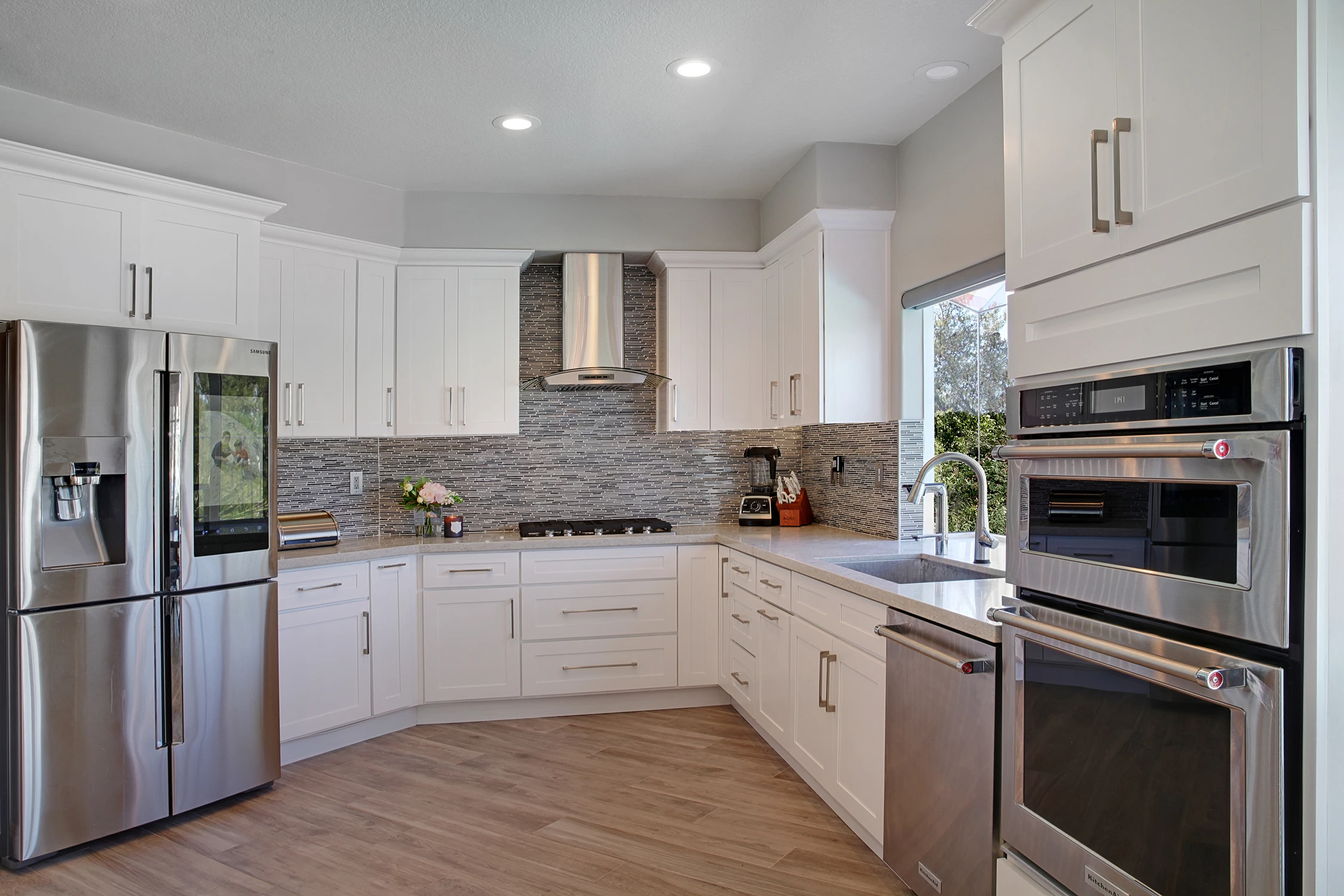 White kitchen with stainless appliances, paneled cabinetry, and wood flooring