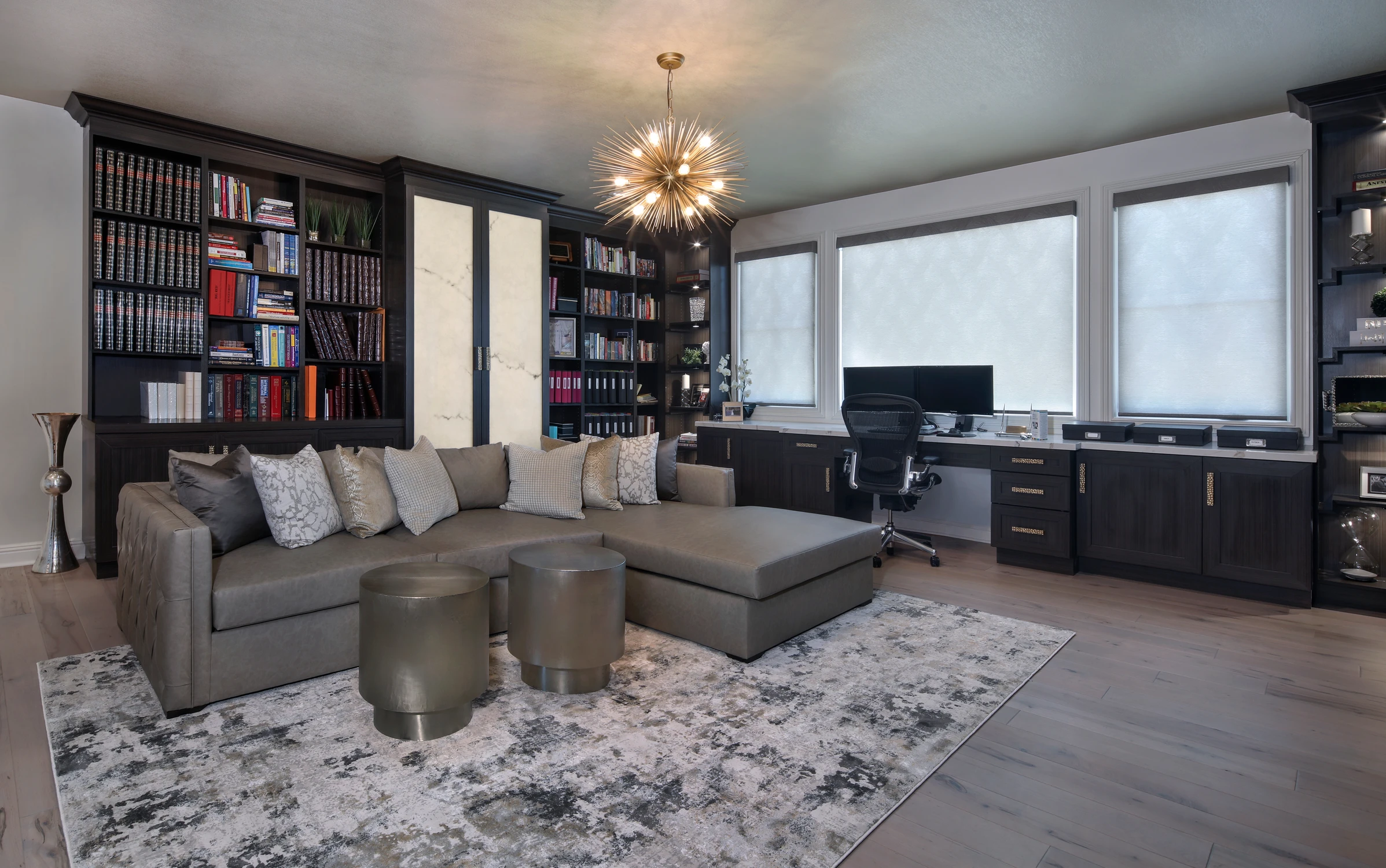 Home office with sectional seating, dark bookcases, and window desk