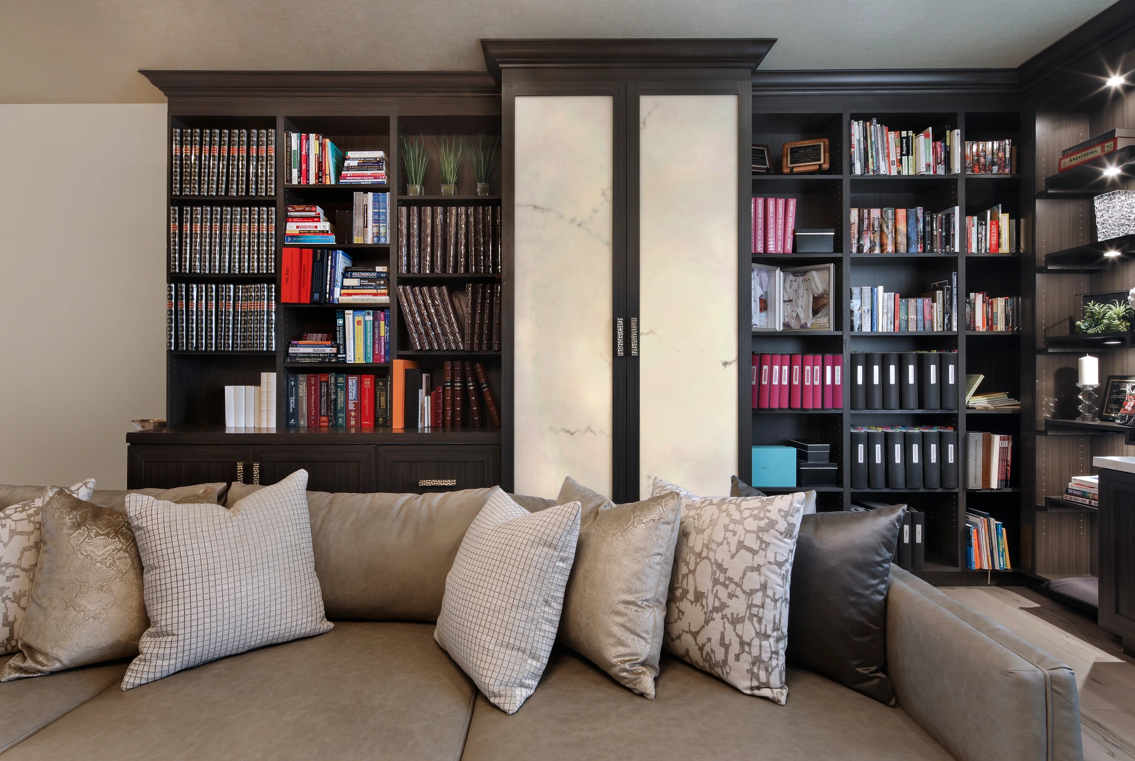 Dark bookcases with marble cabinet panels behind sectional seating