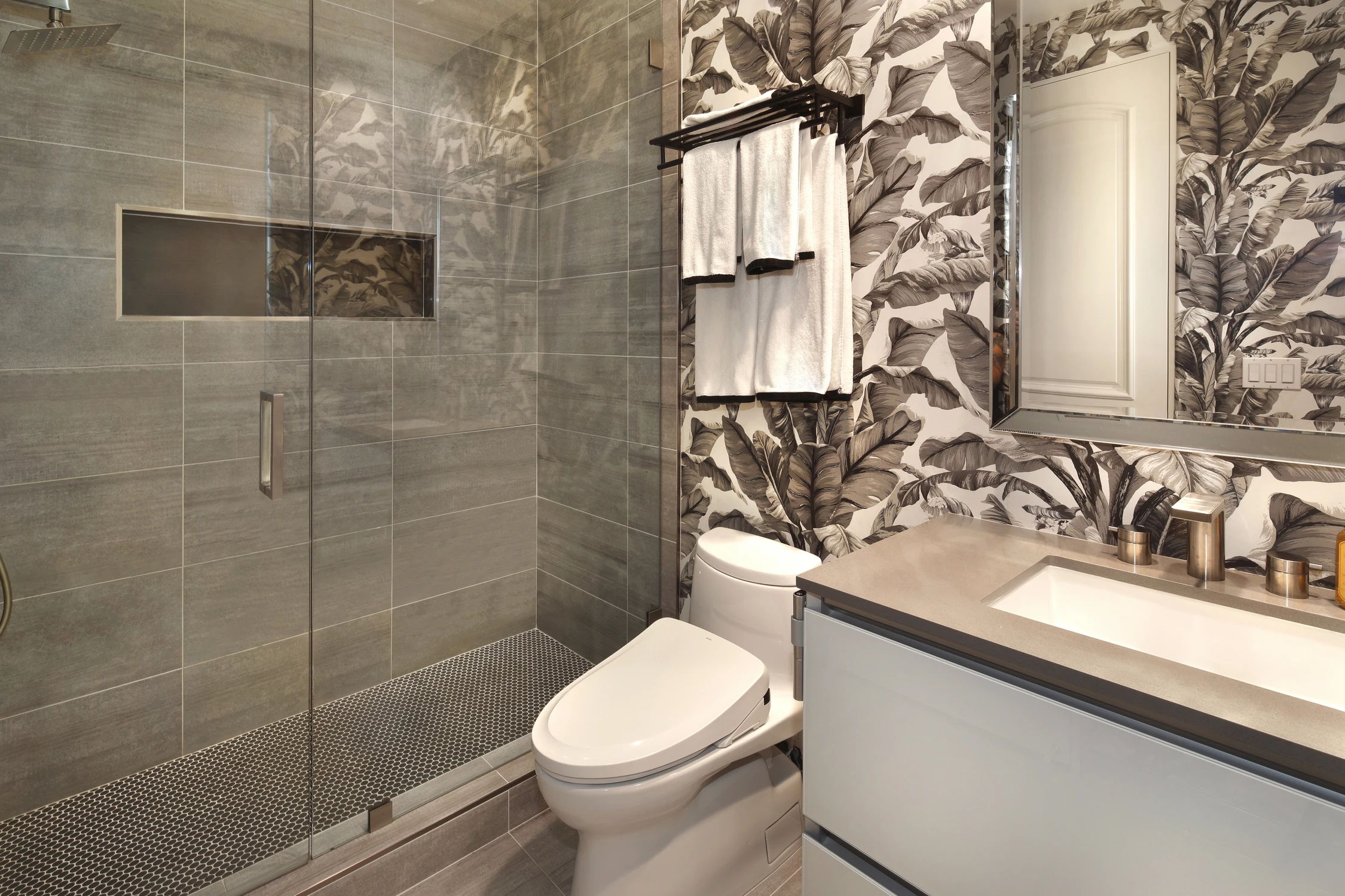 Bathroom with gray tiled shower, white toilet, and botanical wallcovering