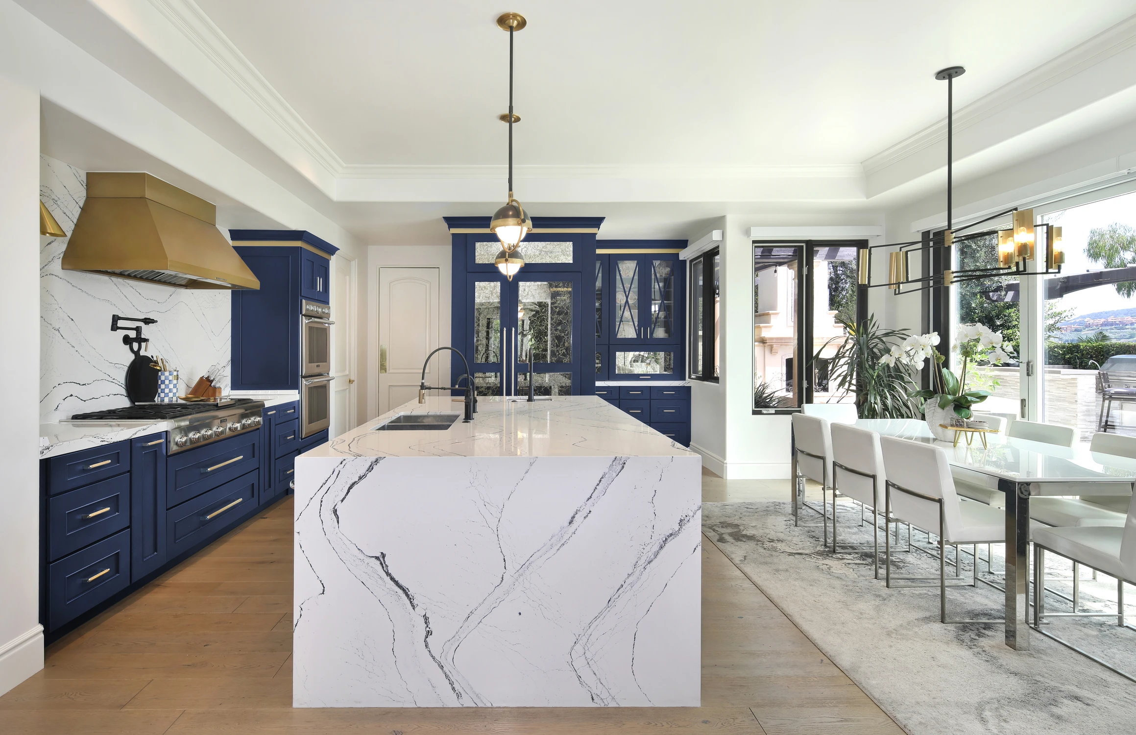 Blue kitchen with white island, brass range hood, and dining area
