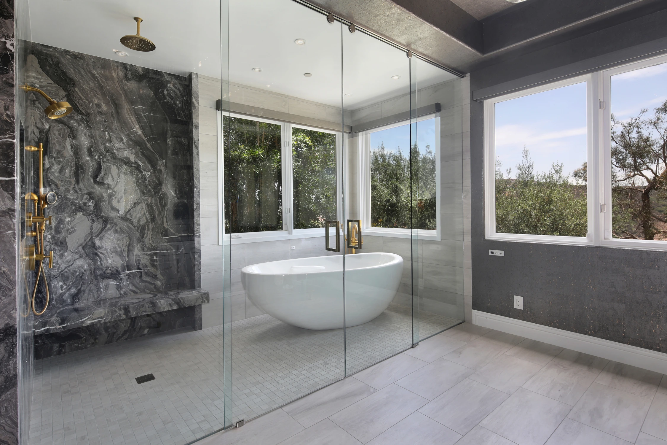 Freestanding tub beside dark stone shower and large windows