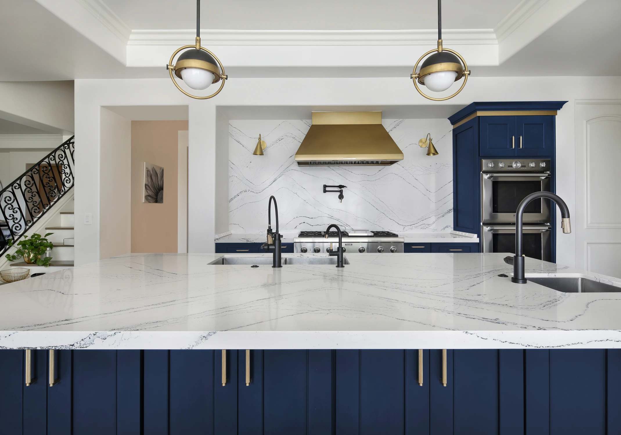 Blue kitchen range wall with brass hood and white veined island