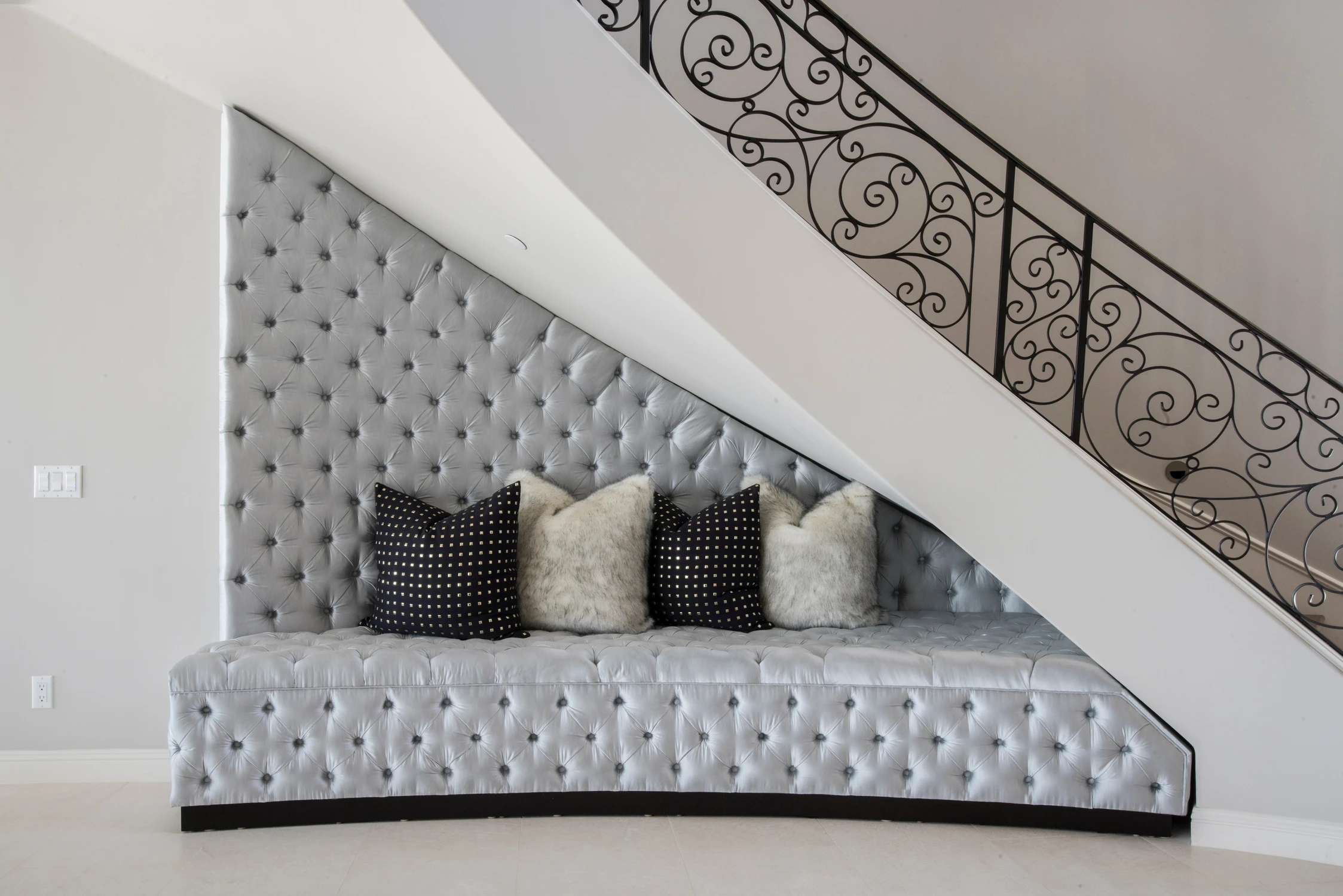 Custom tufted bench beneath a curved staircase