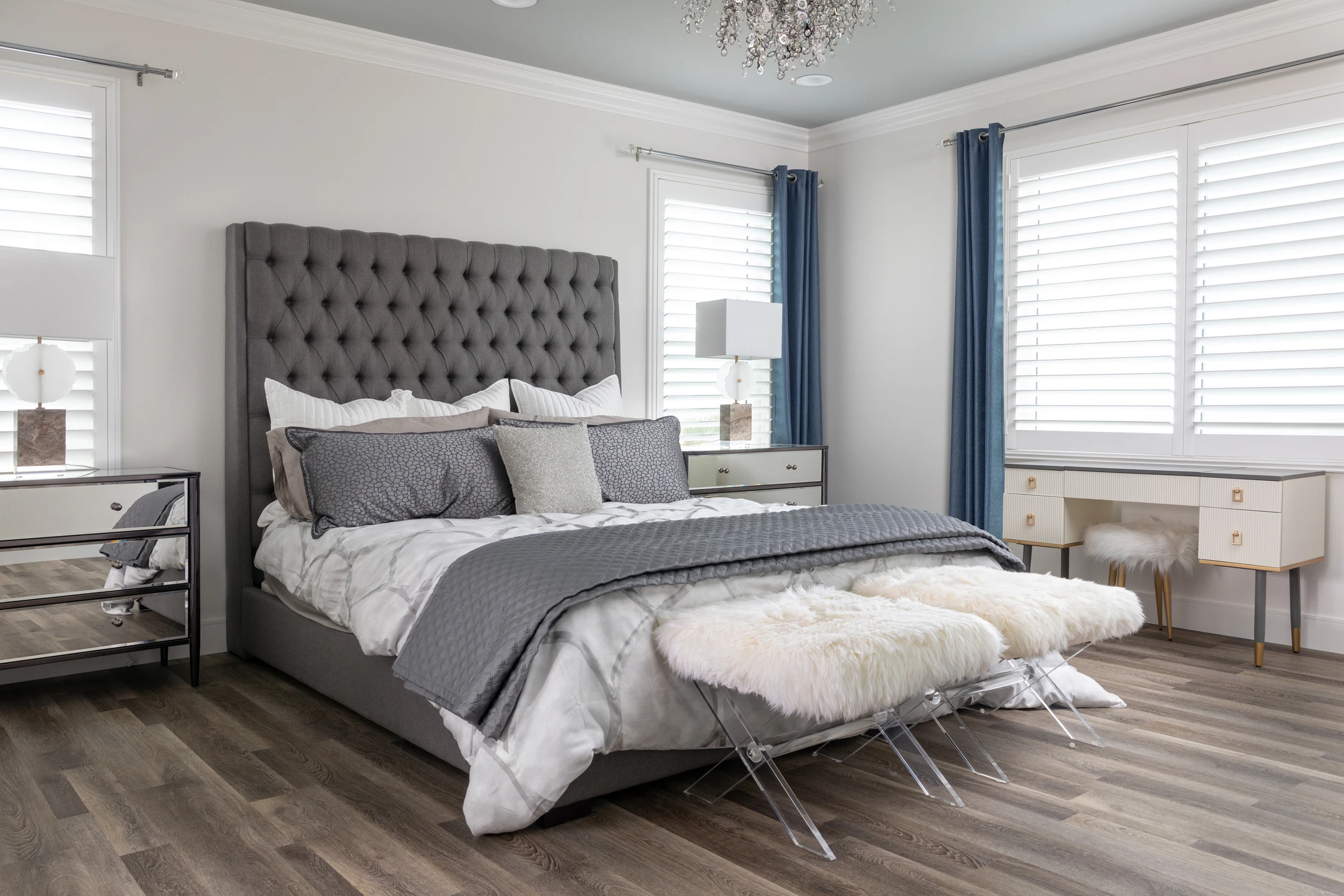 Bedroom with a tufted gray headboard, mirrored furniture, and blue drapery