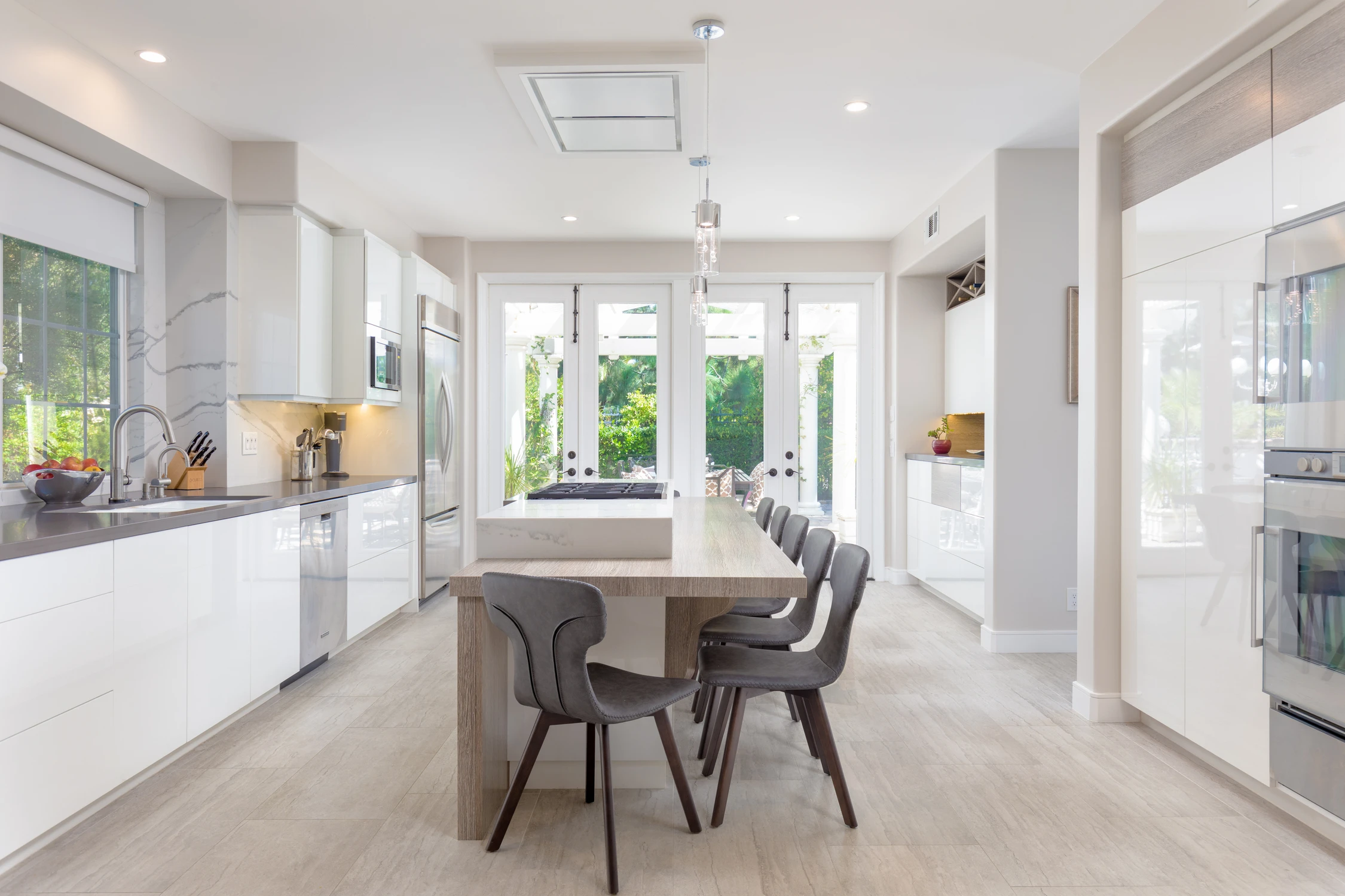 Long white kitchen with central dining table and garden doors