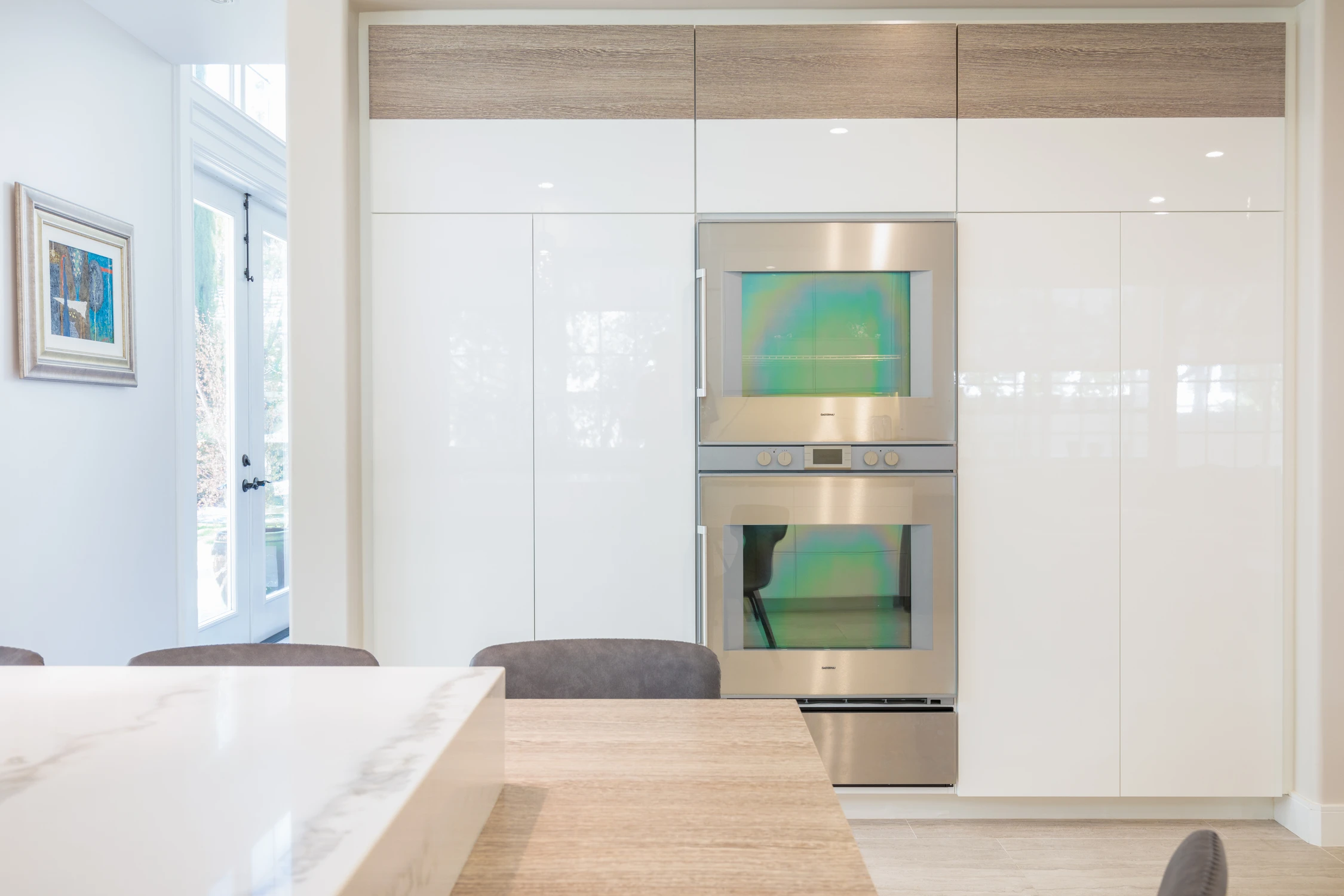 Built-in kitchen appliance wall with glossy white cabinetry and wood shelf