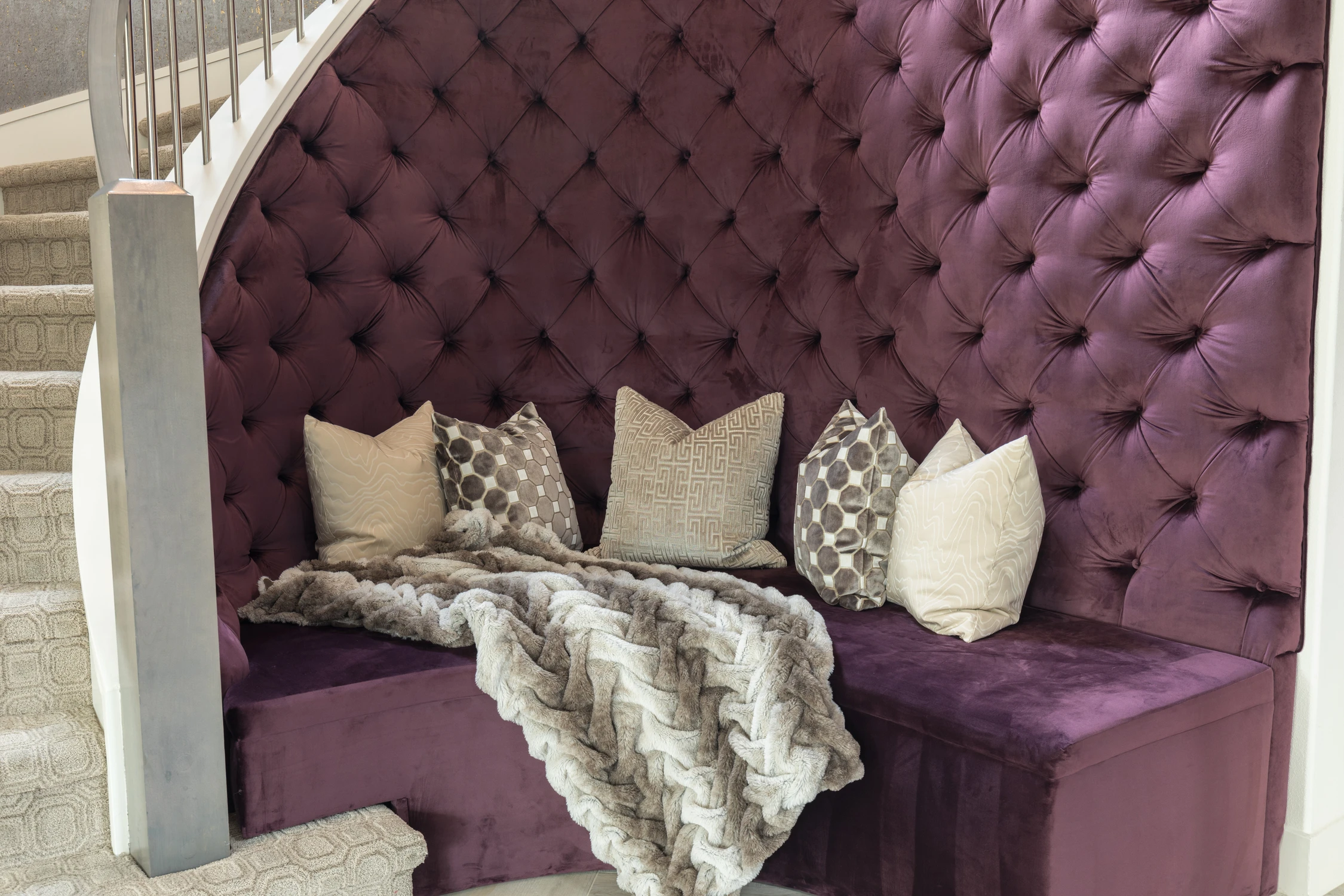 Plum tufted entry bench under curved staircase and pale stone floor