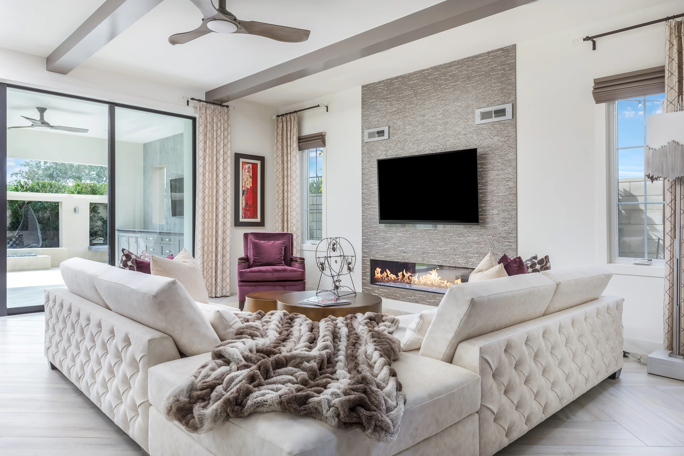 Bright family room with white sofas, stone fireplace, and tall windows