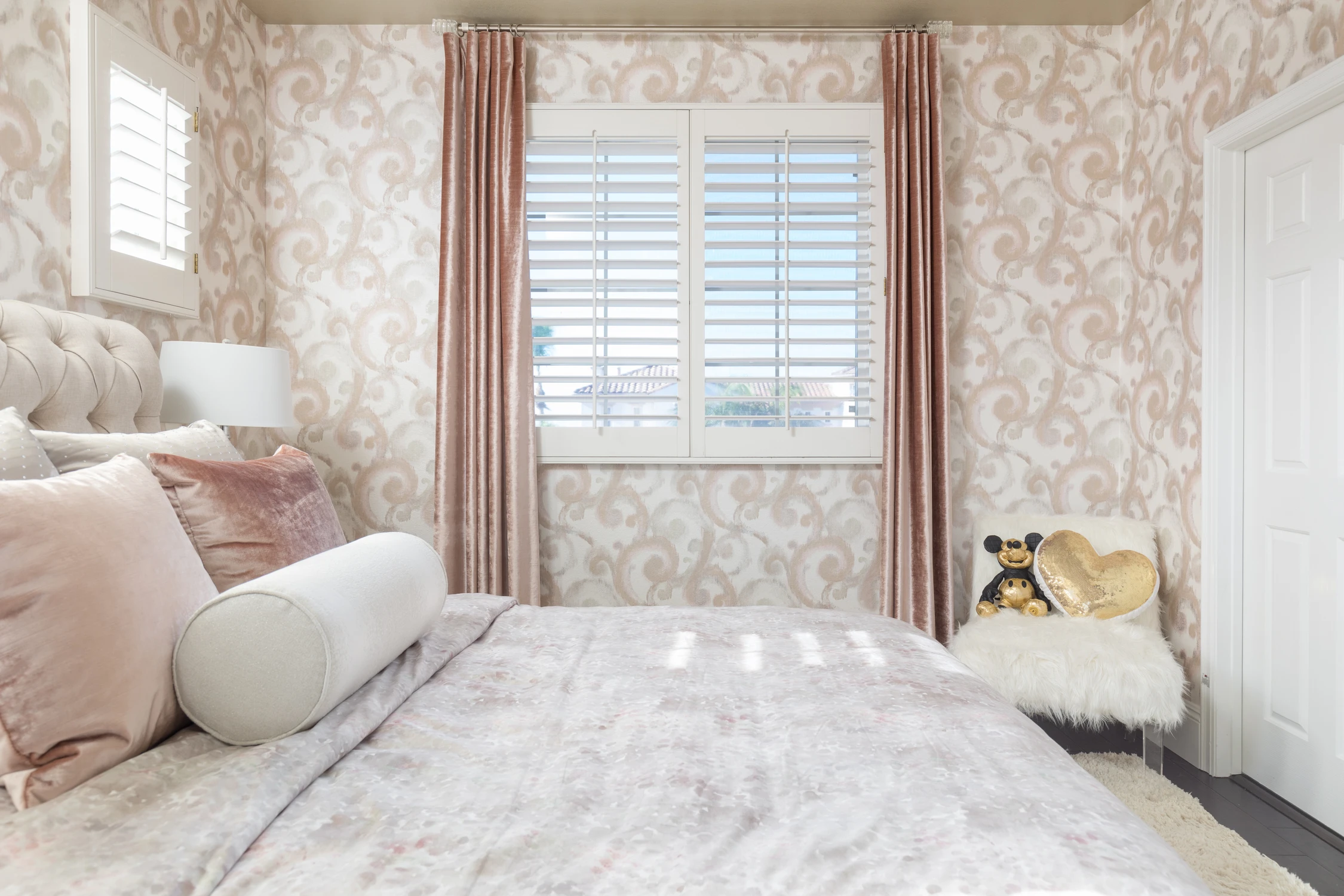 Tufted bed with round bolster pillow and floral wallcovering