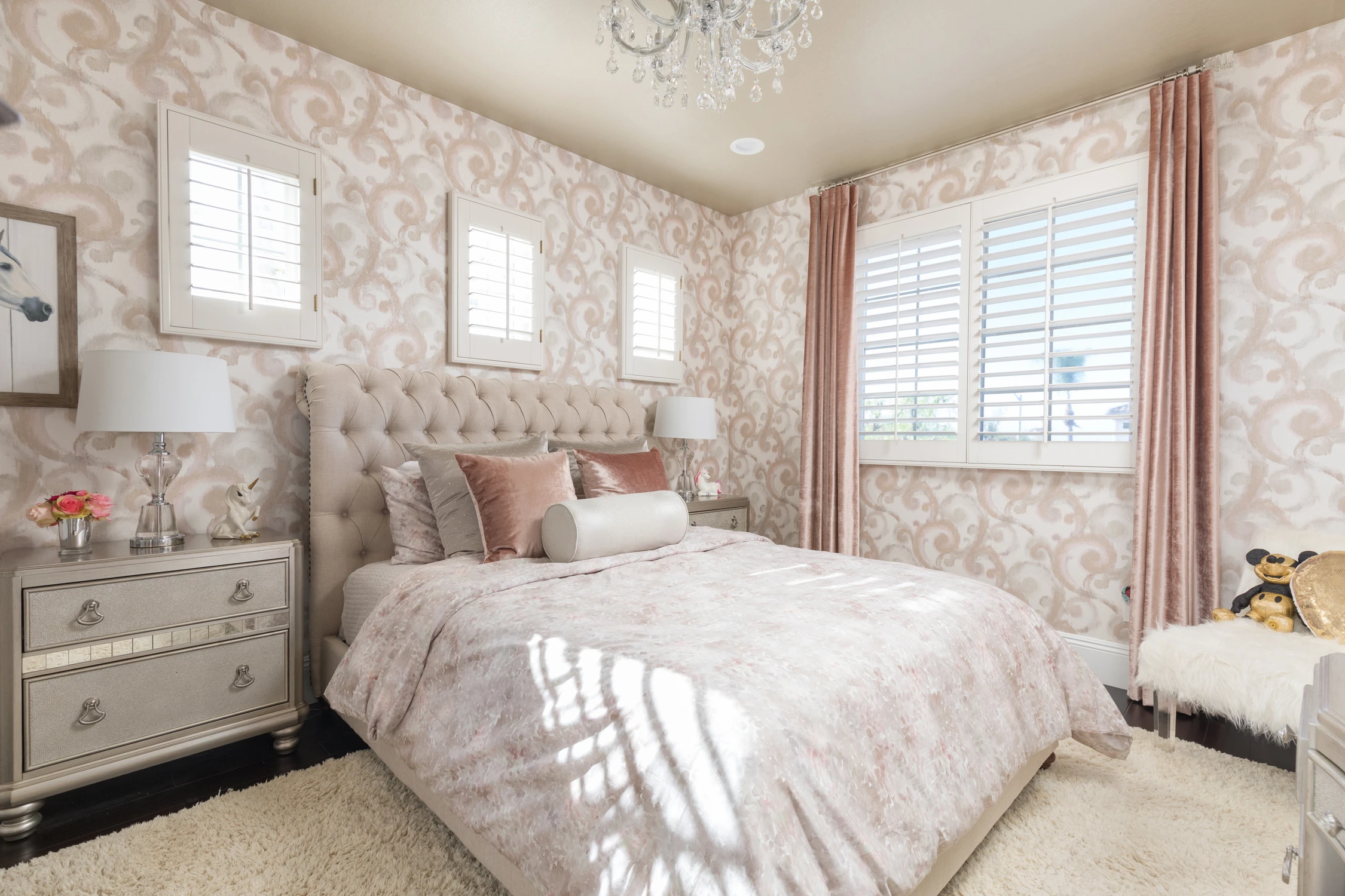 Bedroom with tufted bed, mirrored dresser, and pink curtains