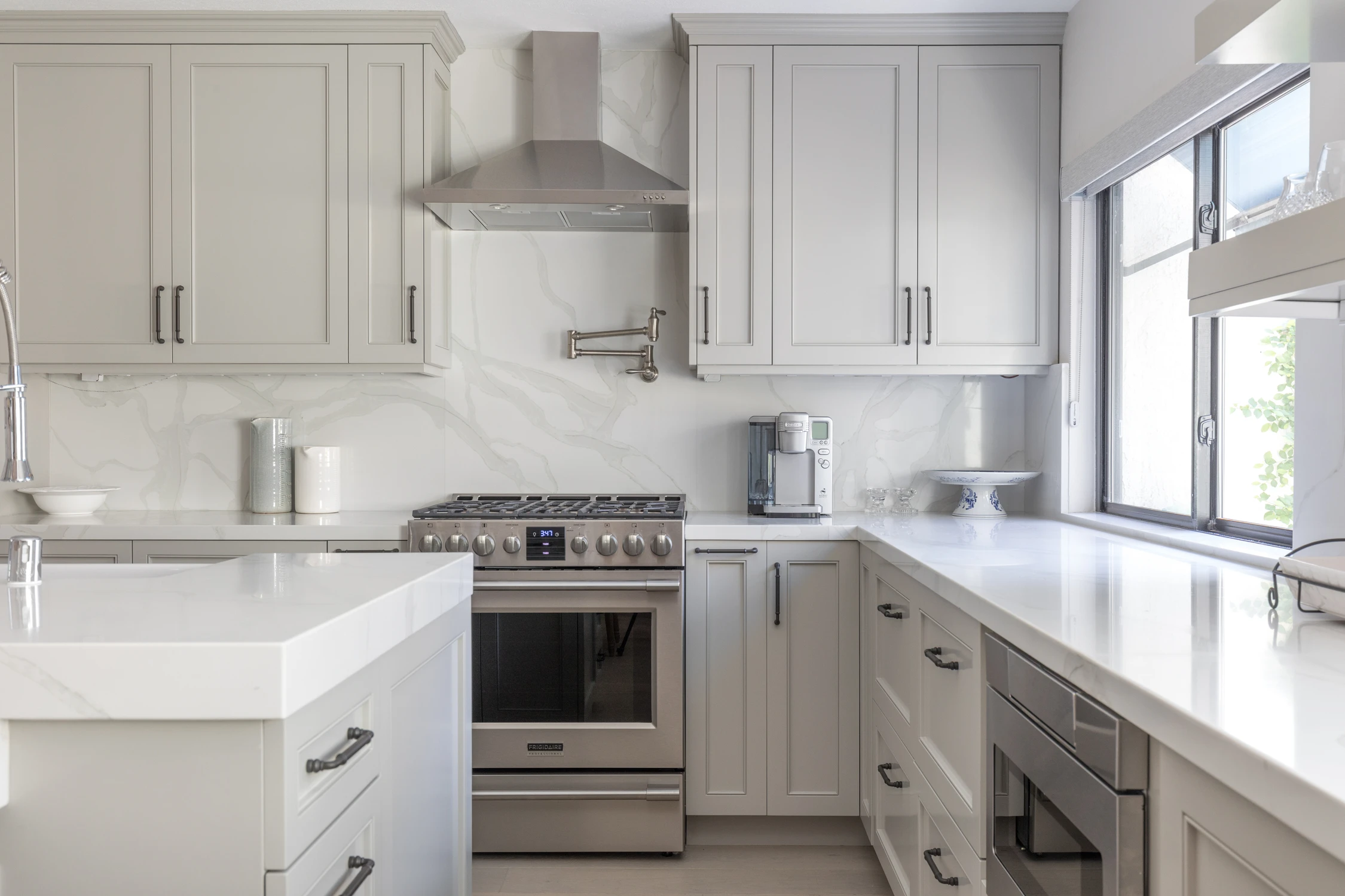 White kitchen range wall with stainless appliances and pale gray cabinets