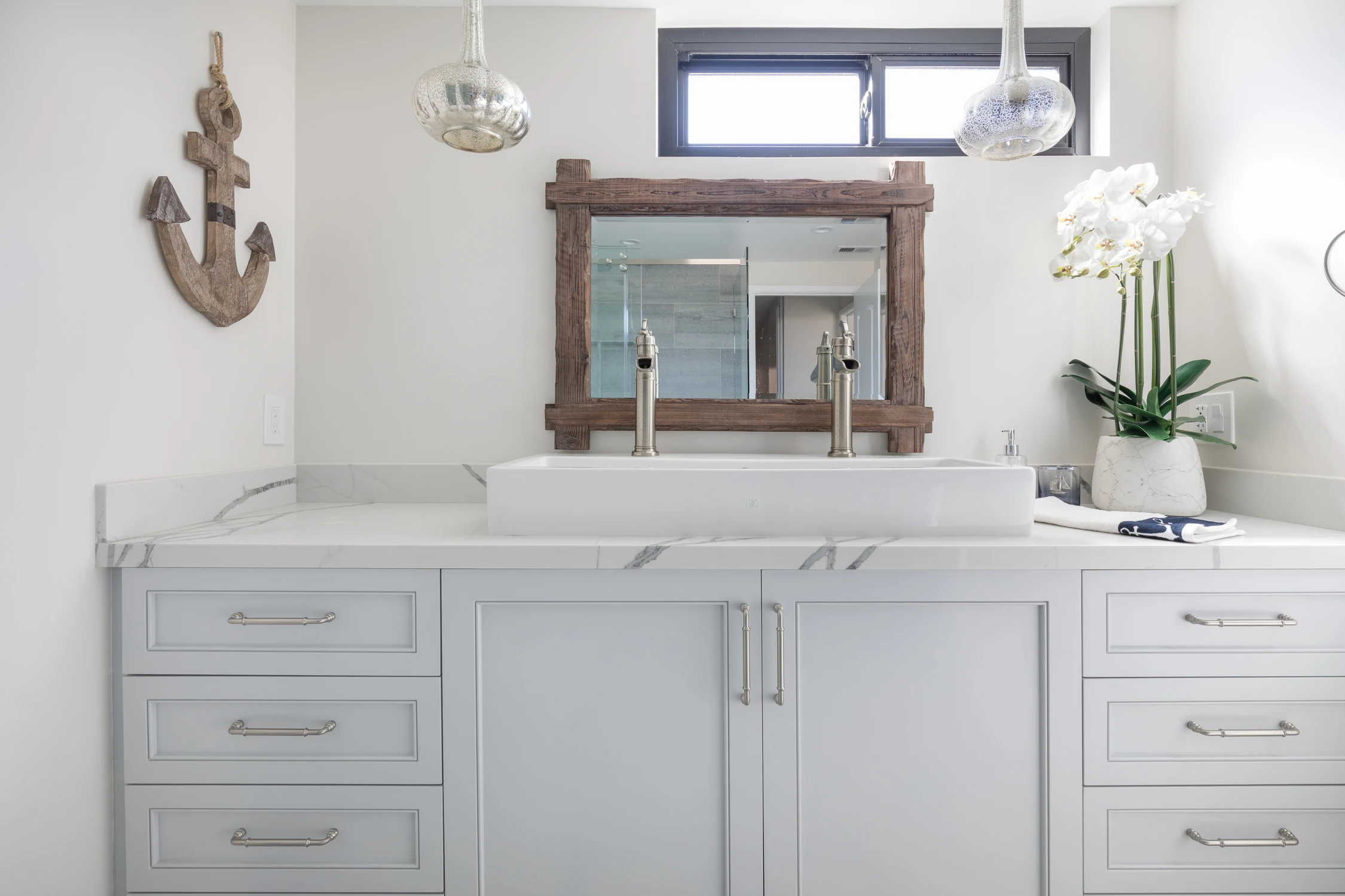 Bathroom vanity with weathered wood mirror, white cabinet, and anchor wall art