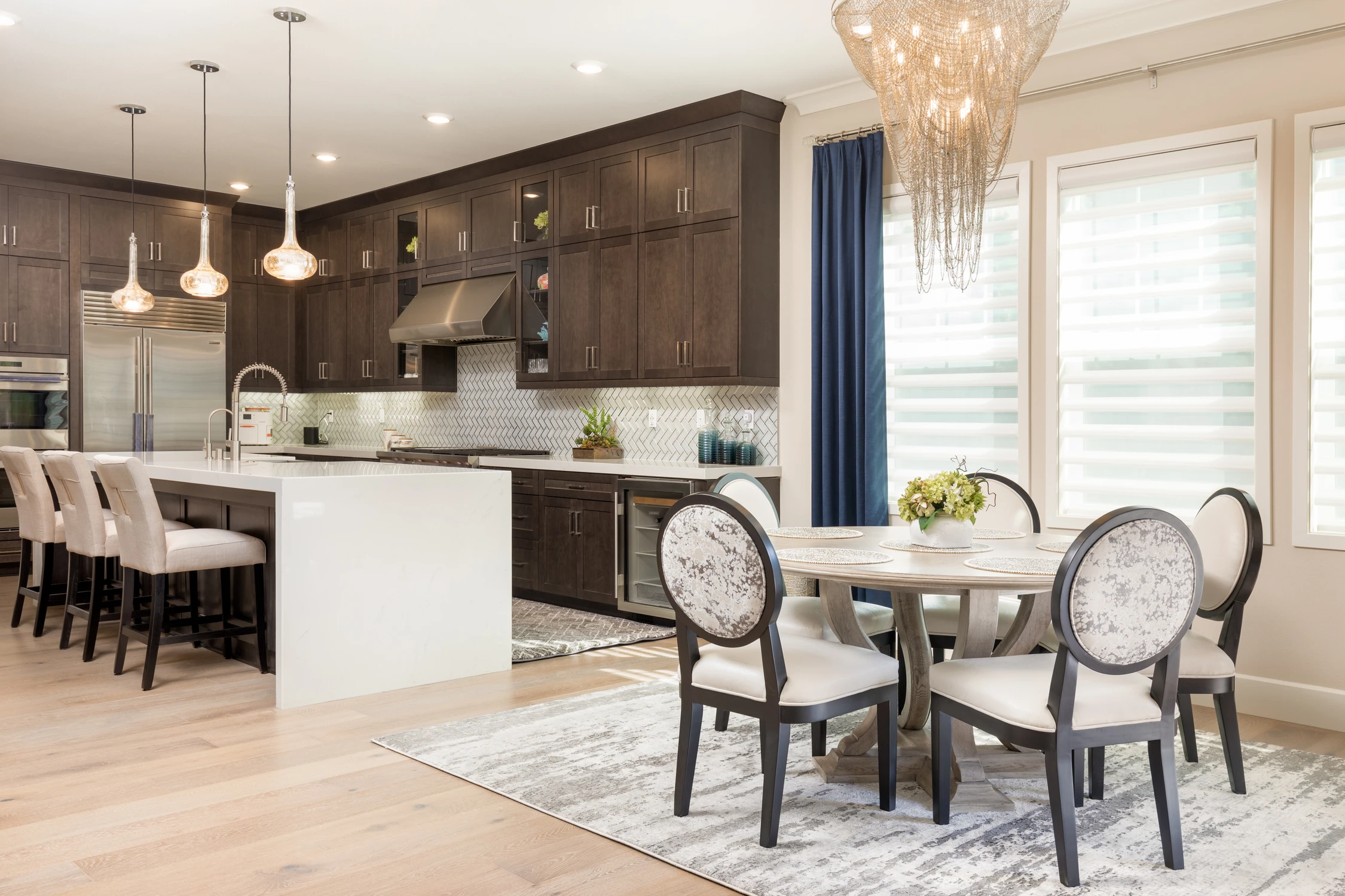 Dark kitchen with white island, dining table, and cascading chandelier
