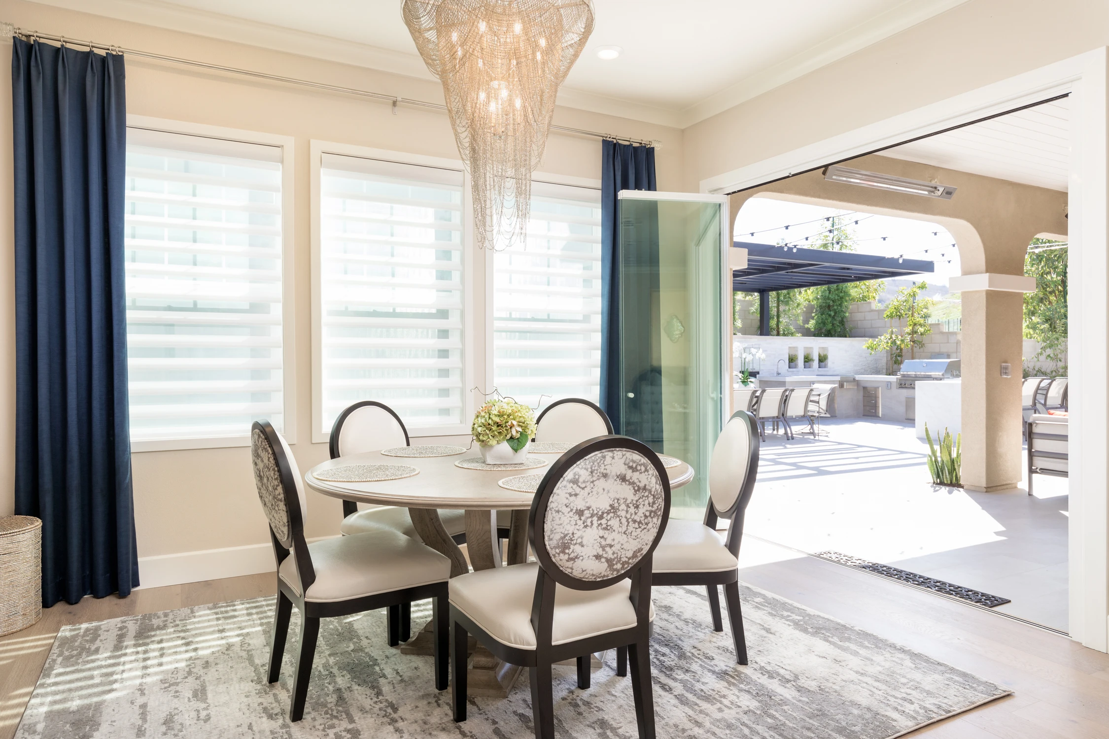 Dining table below crystal chandelier beside blue curtains and open doors