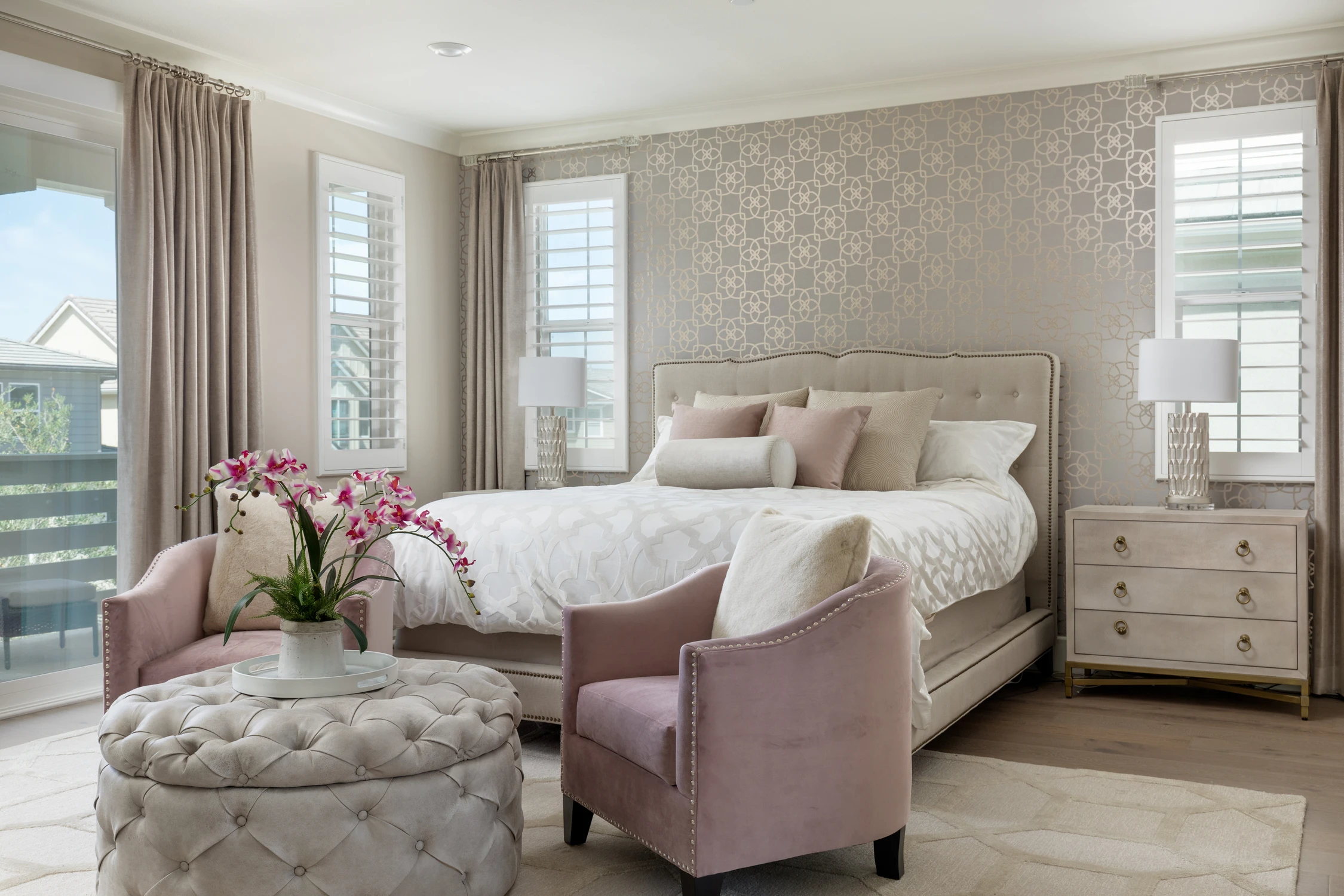 Bedroom with pale upholstered bed, pink chair, and tufted ottoman