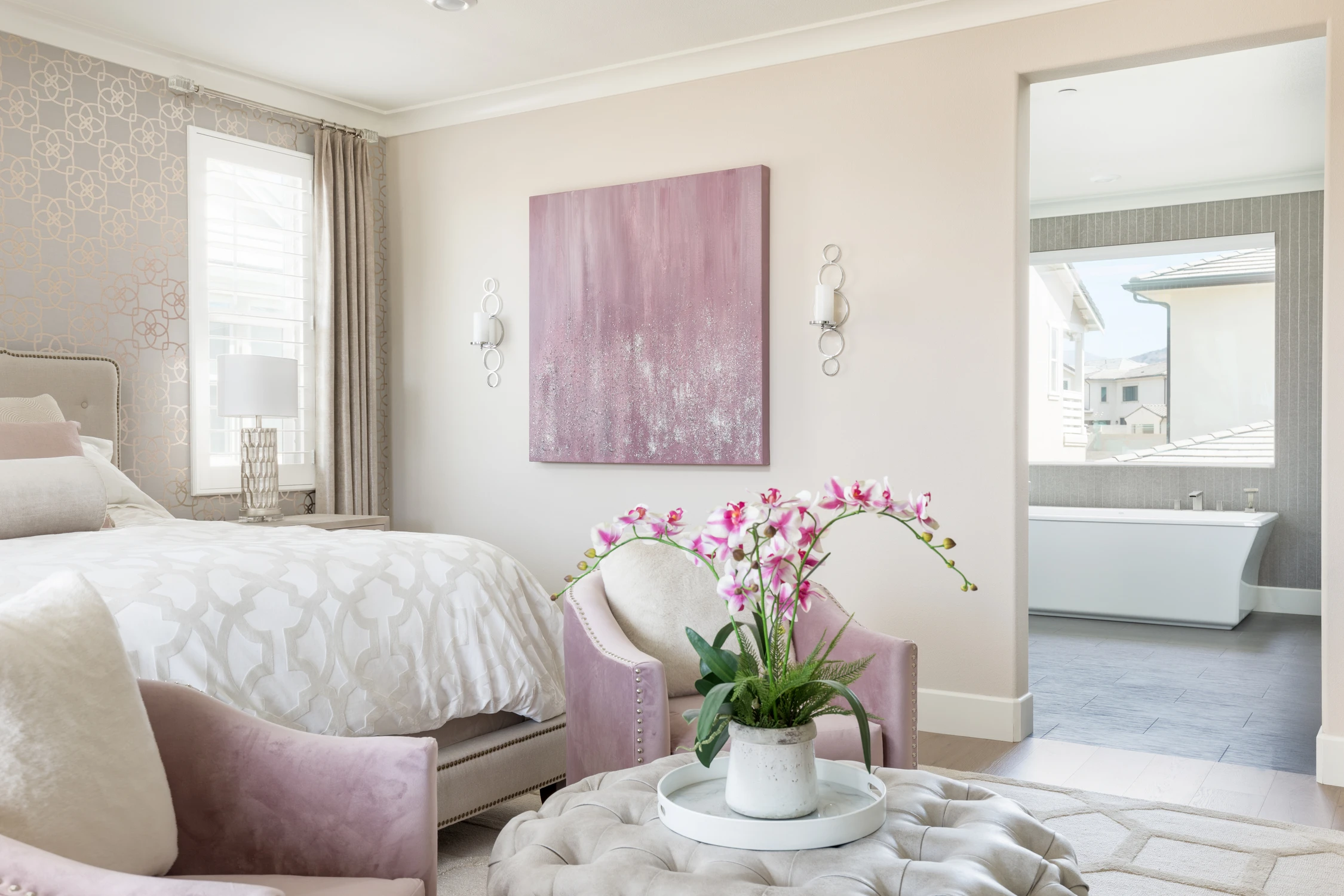 Bedroom seating nook with pink chair, abstract art, and open bath doorway