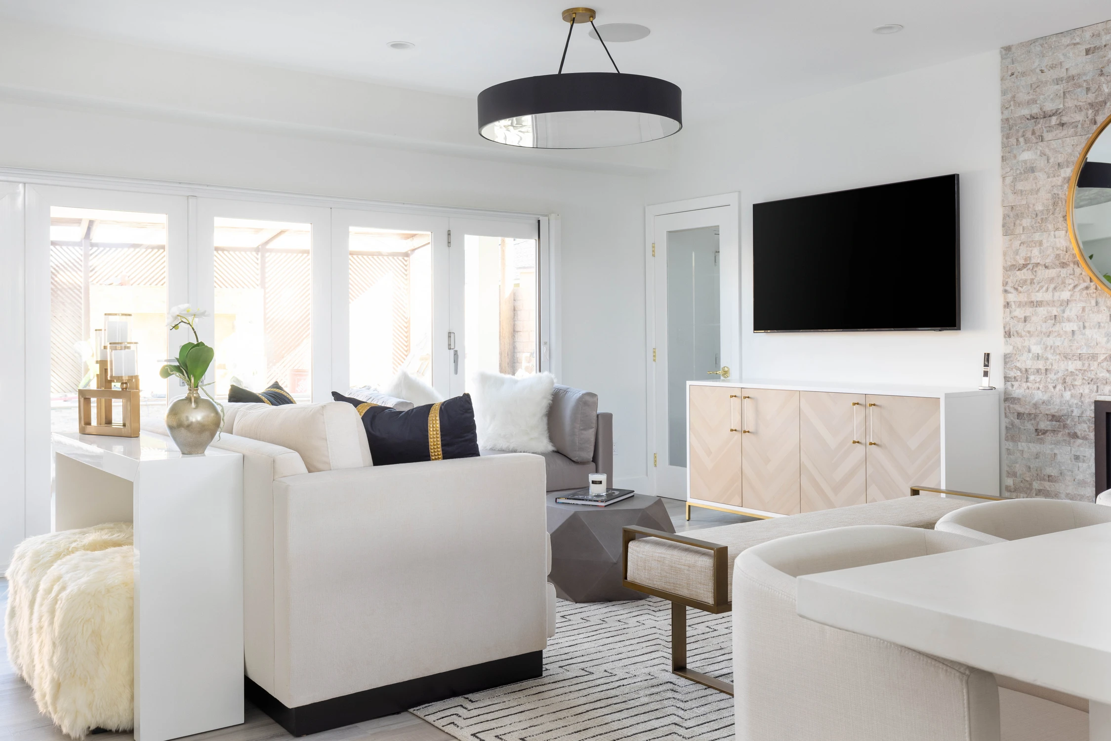 Open living room with white seating, television, and stacked-stone fireplace